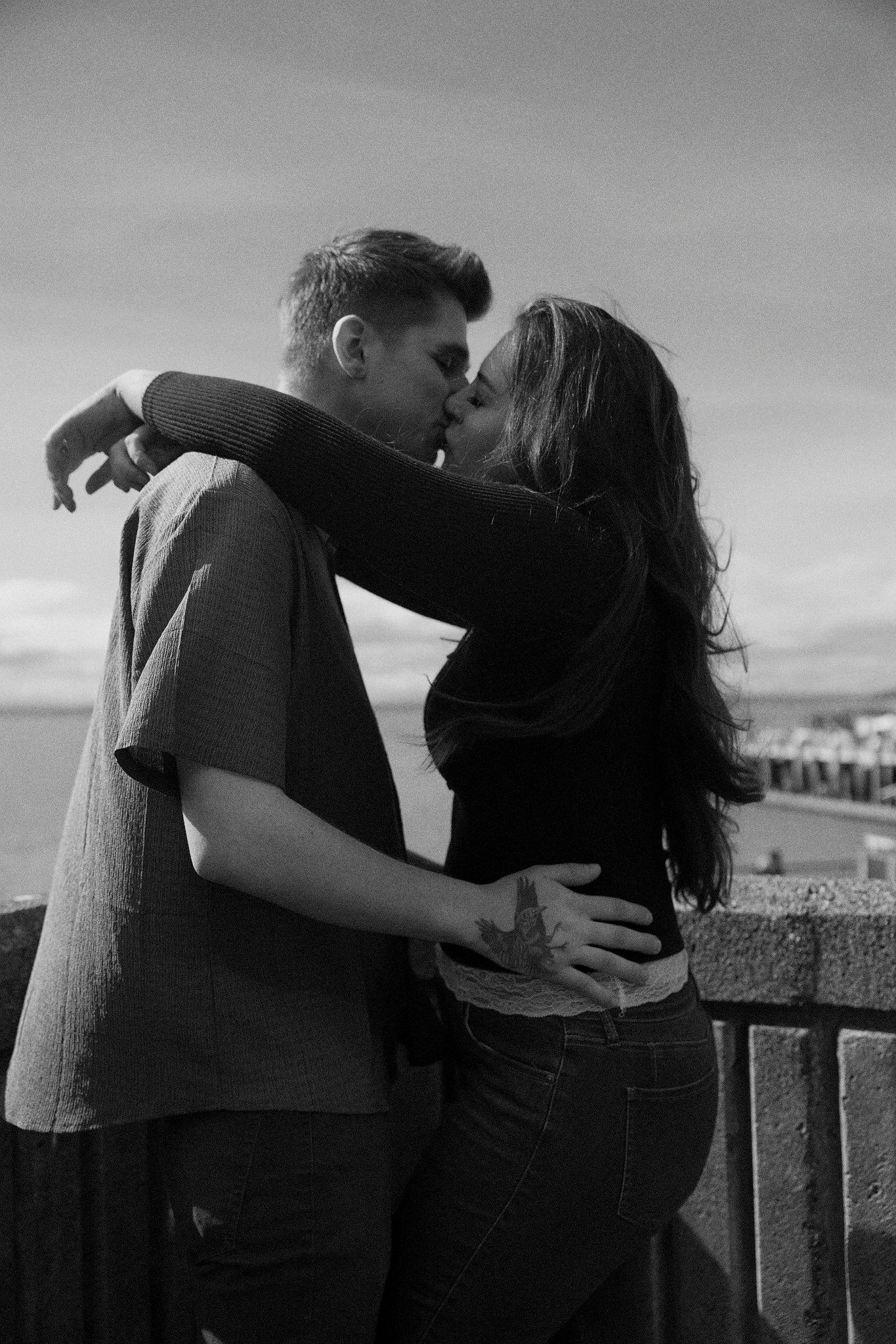 A romantic black and white photo sequence showing a couple embracing and kissing on a seaside boardwalk.