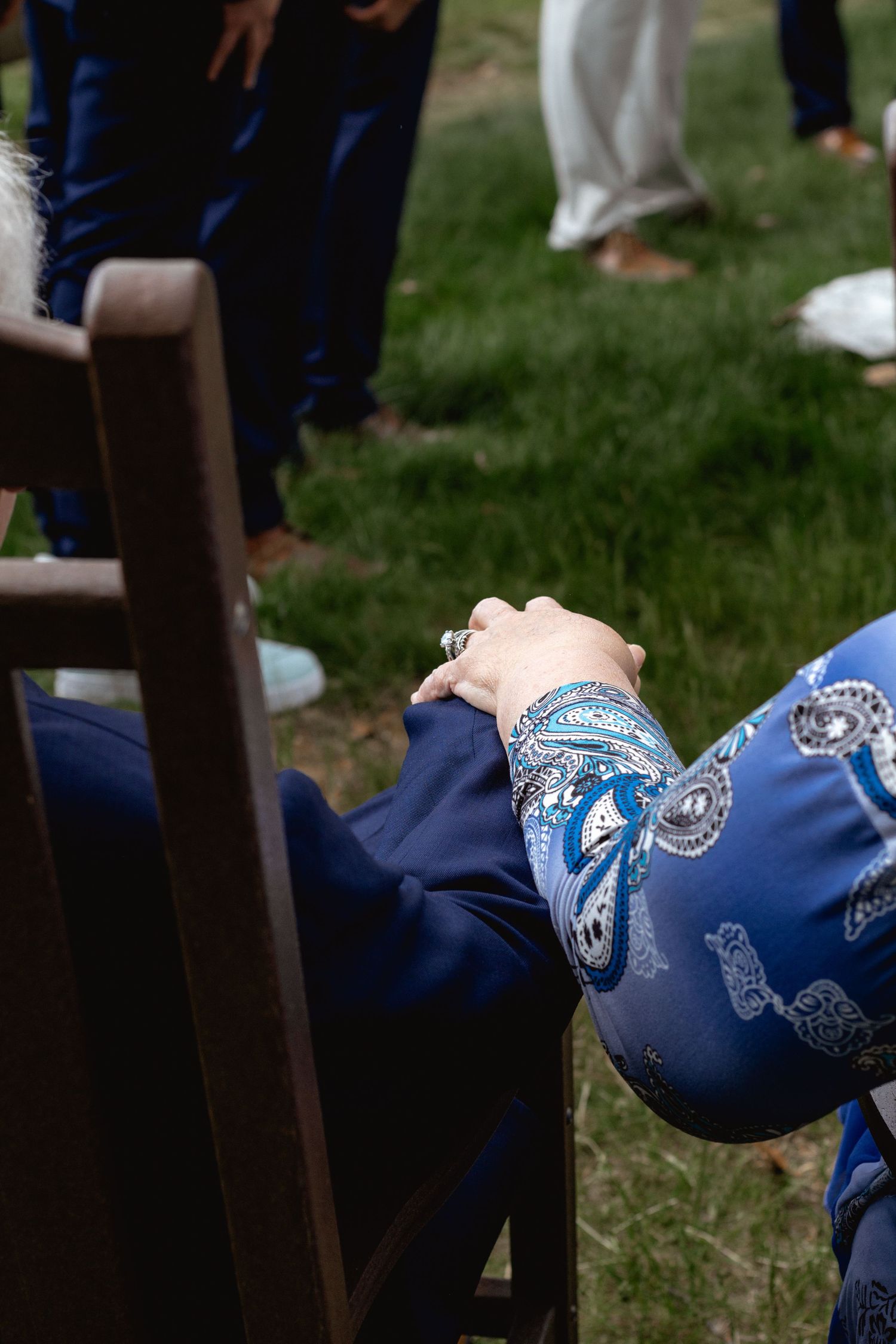 Close-up of someone wearing a blue patterned bandana and silver bracelets resting their hand on a wooden chair outdoors.