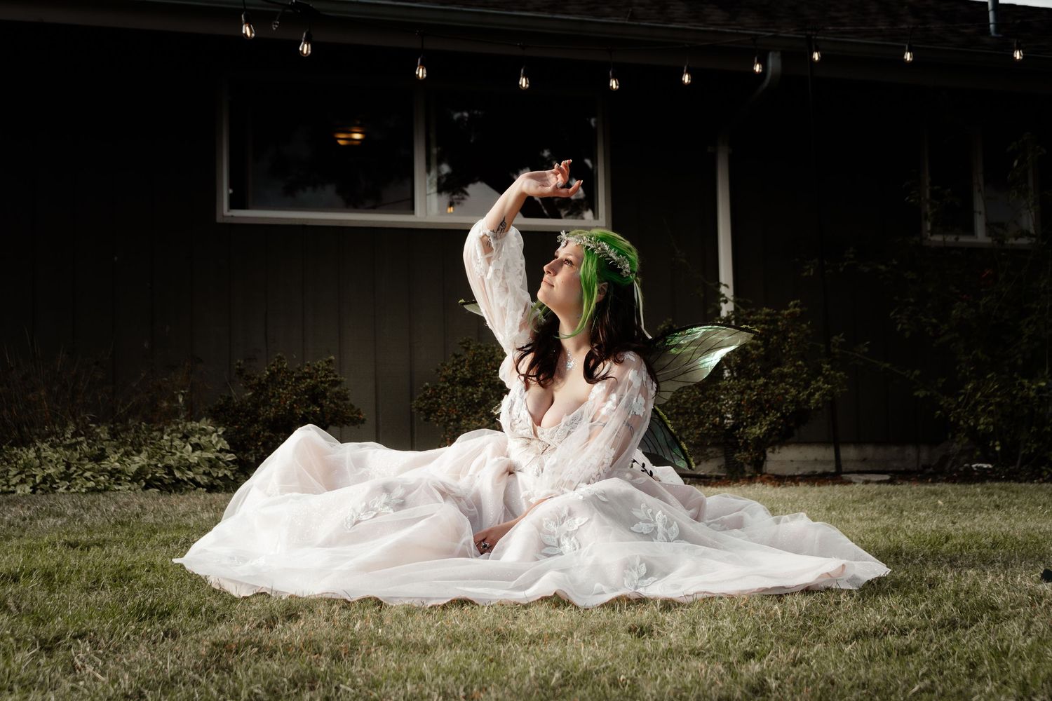 A romantic wedding couple sits together on grassy lawn in elegant white dress and suit at dusk.