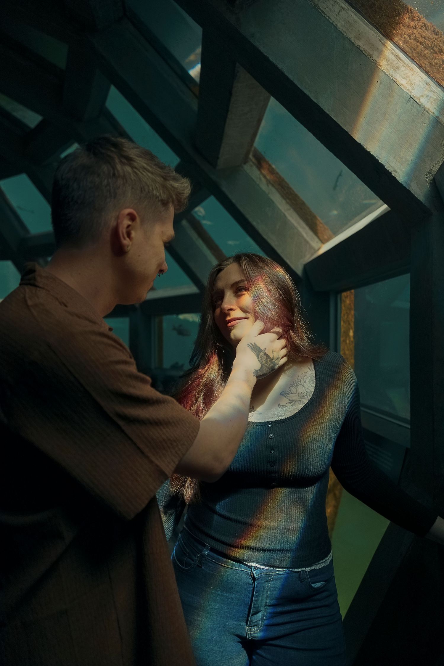 A romantic couple embraces in a dimly lit stairwell with dramatic lighting and shadows.