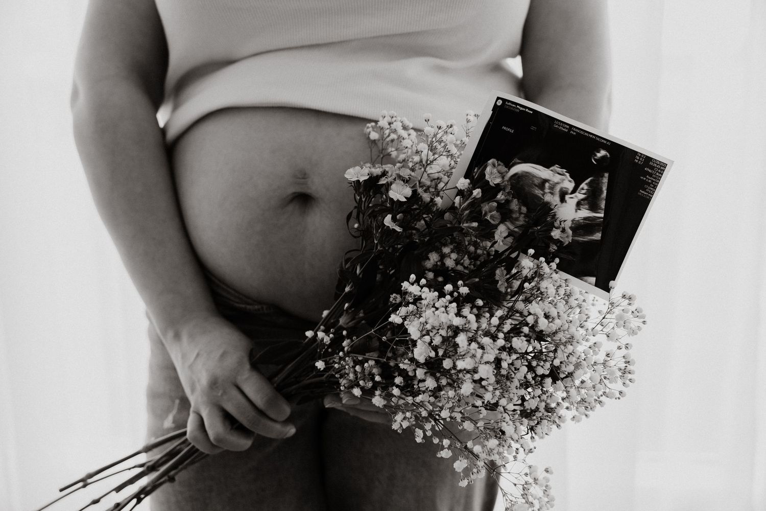 Pregnant woman holding baby's breath flowers and ultrasound photo, black and white maternity photography.