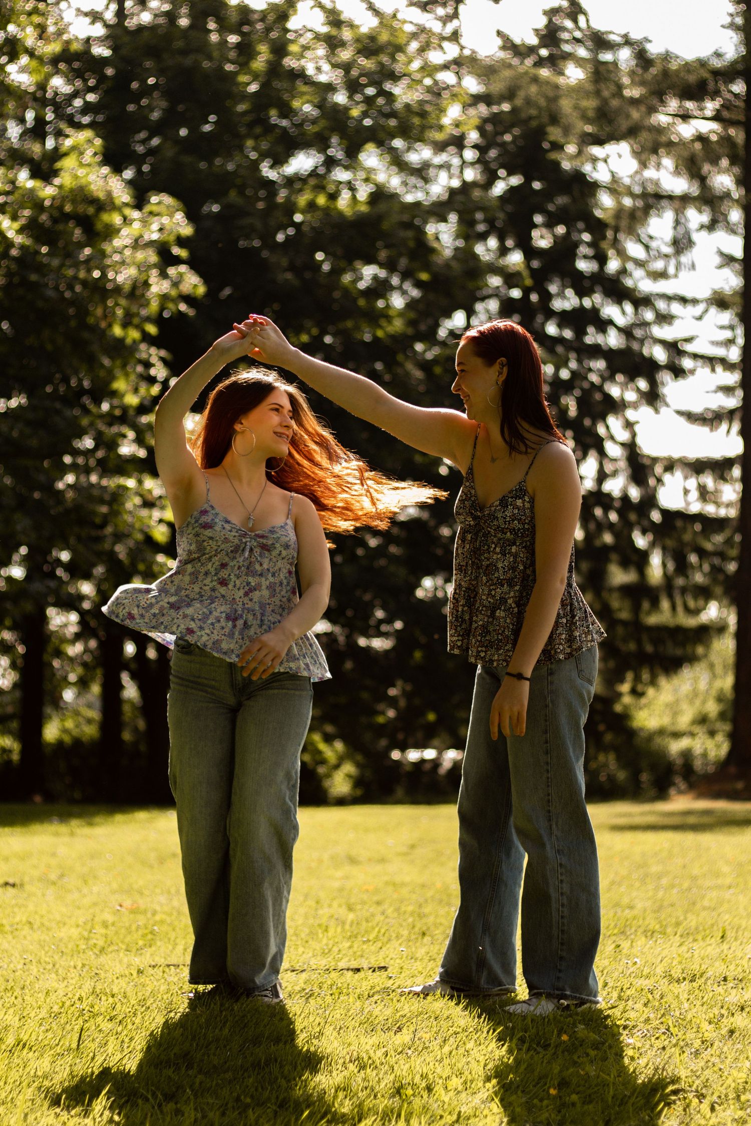 A couple dancing and embracing in a sunlit meadow with evergreen trees in the background during golden hour.