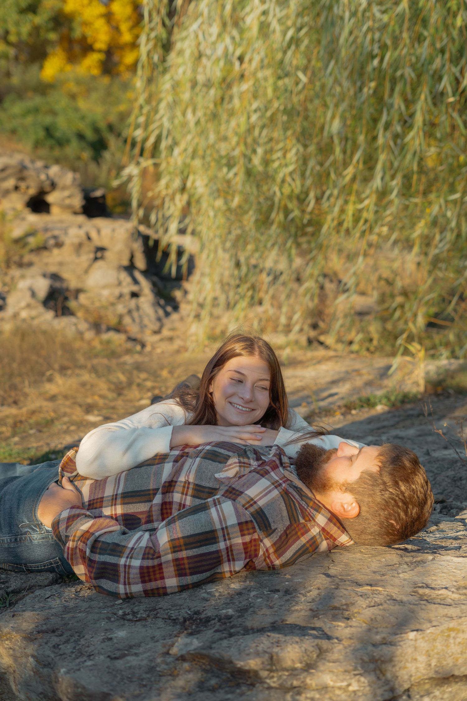 A couple lying on a rock formation at sunset wearing plaid and casual attire.