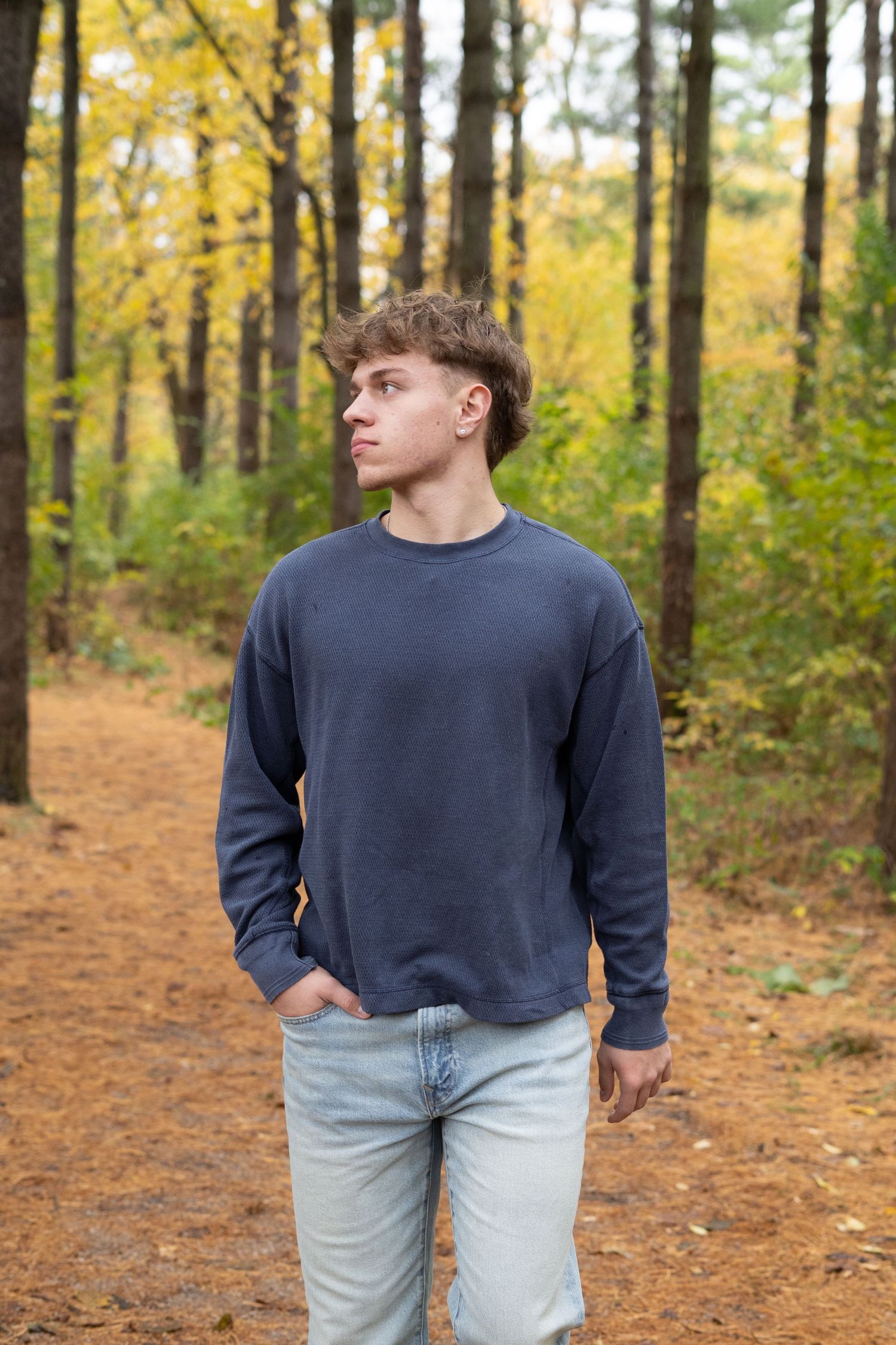 A person in a navy sweater and light jeans walks along an autumn forest trail with golden foliage.