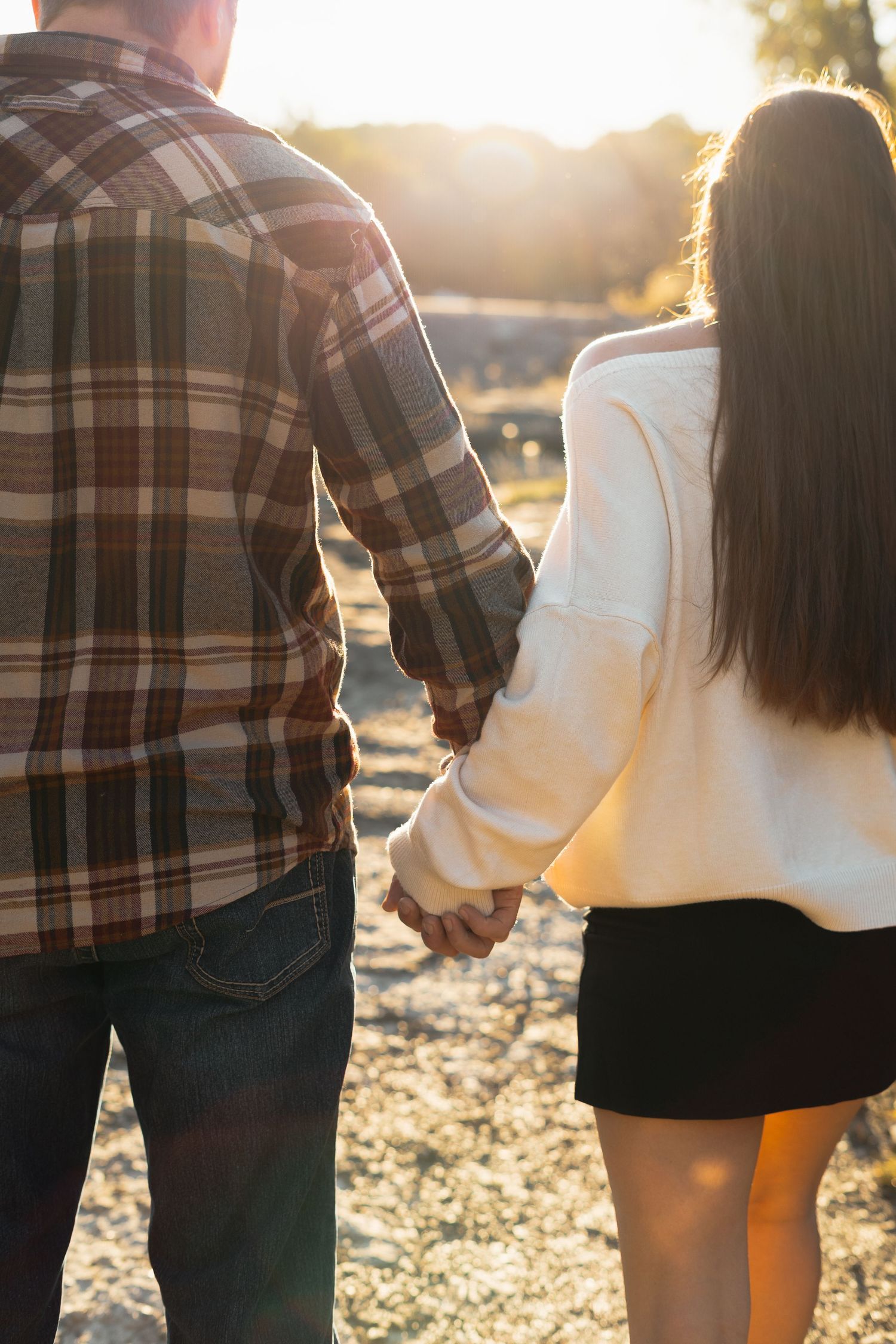 Couple holding hands at sunset with warm backlighting in casual autumn outfits.