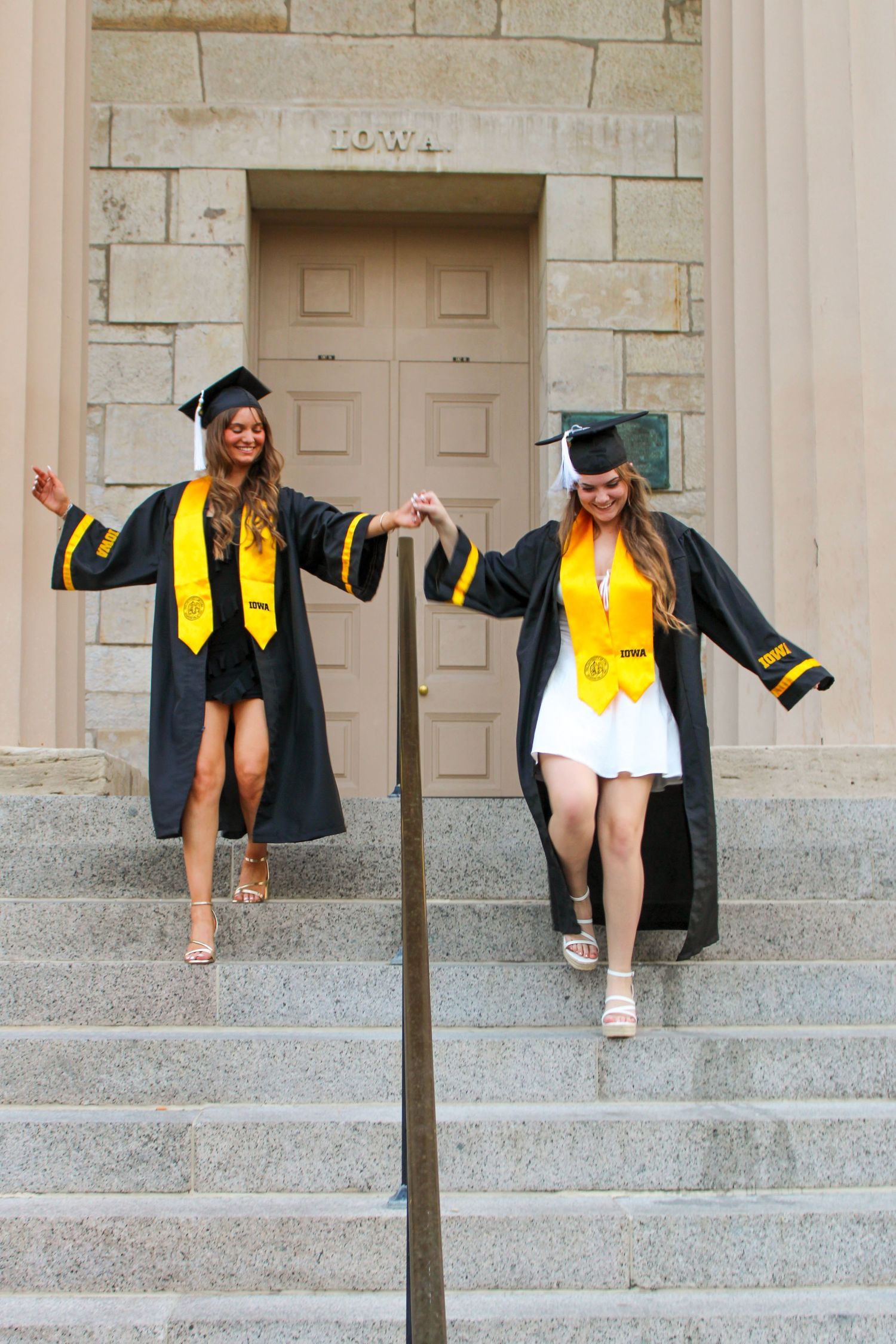 Graduate in cap and gown descending stone steps in celebratory poses.
