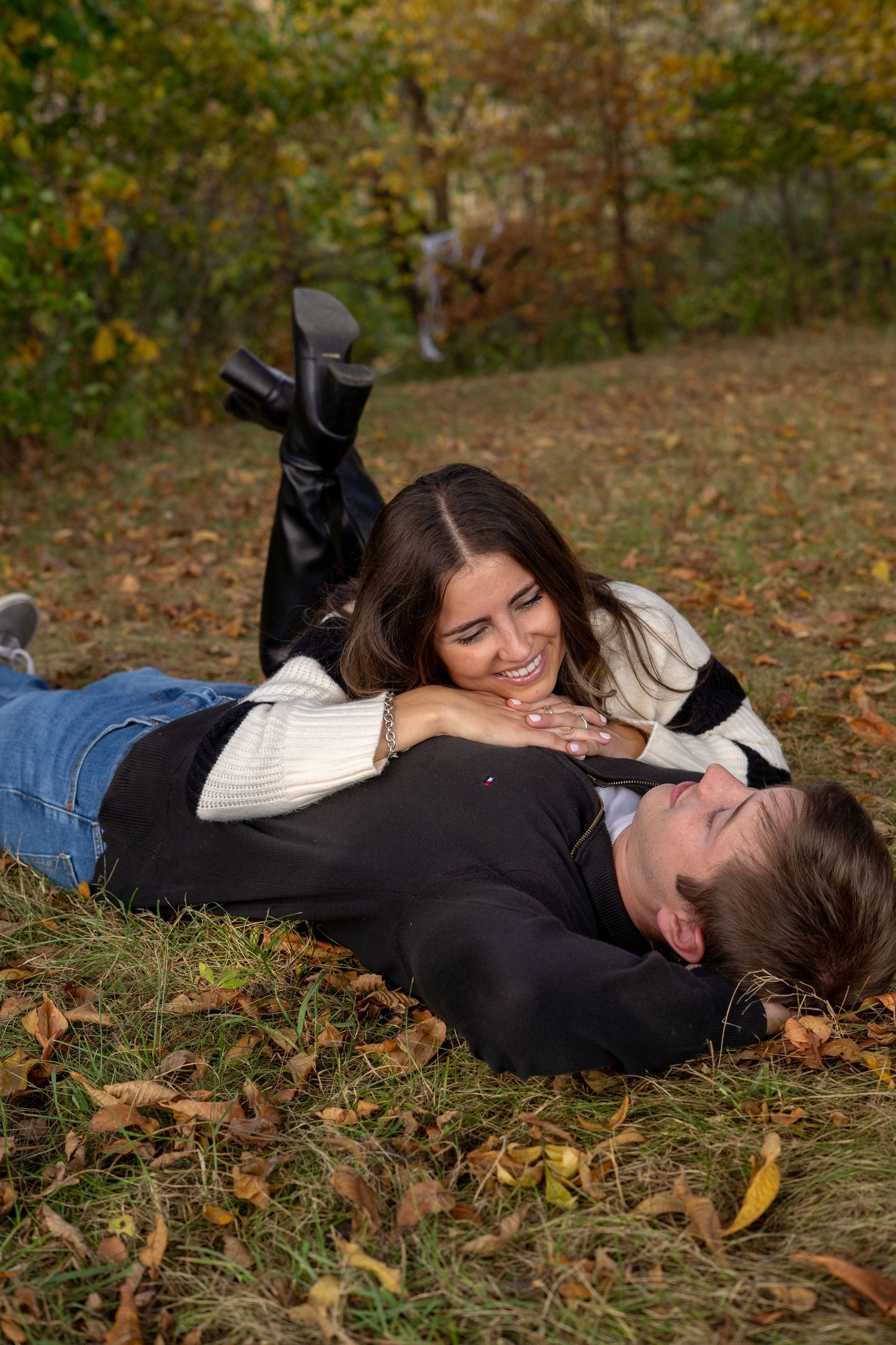 Two people rest together on fallen leaves during autumn.