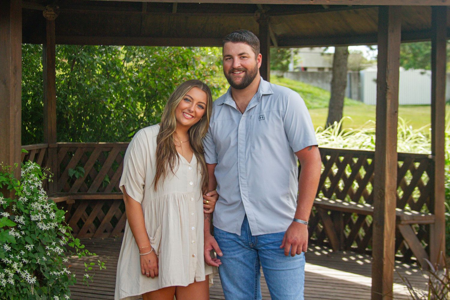 A happy couple posing together on a wooden porch with greenery in the background.