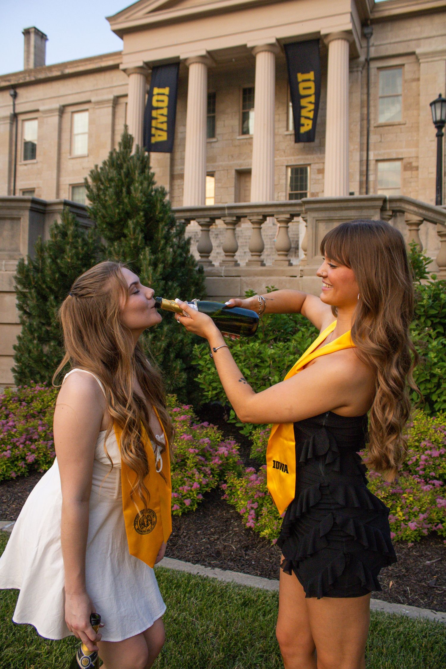 Two friends sharing drinks and posing in front of a grand stone building with columns.