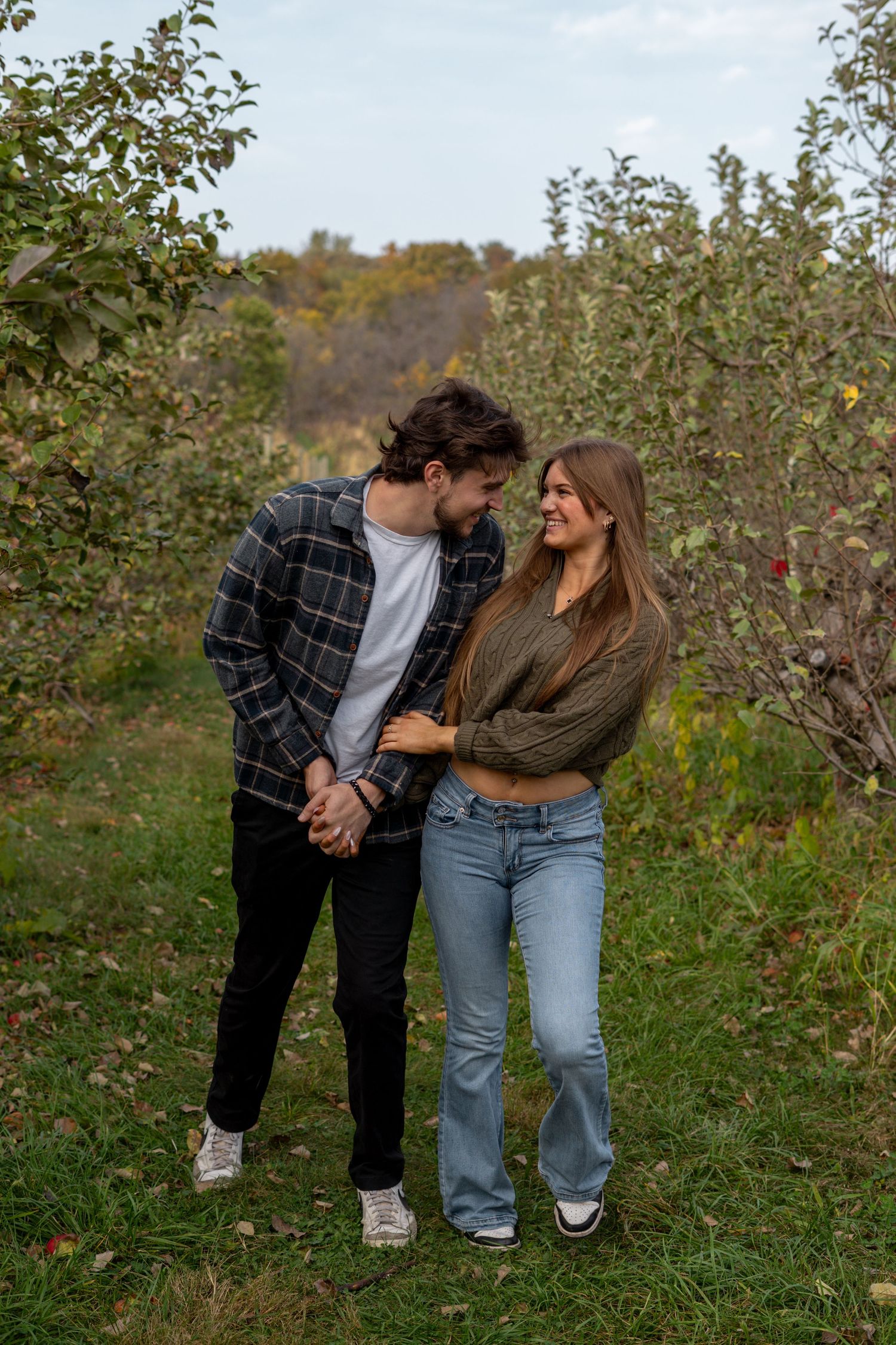 A couple shares a joyful moment together while standing in an apple orchard on an autumn day.