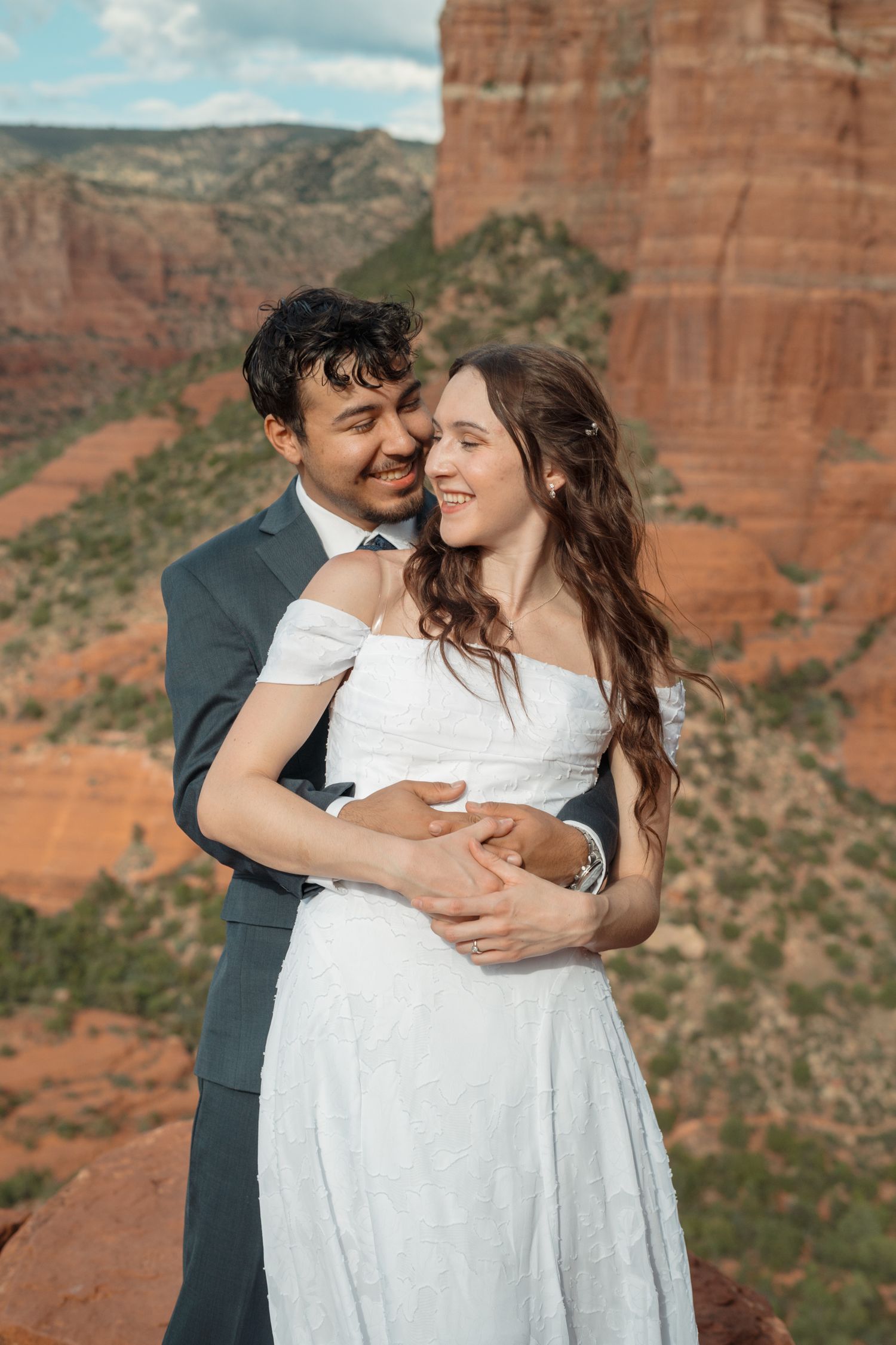 Couple embraces in wedding attire with stunning red rock formations of Sedona, Arizona in the background.