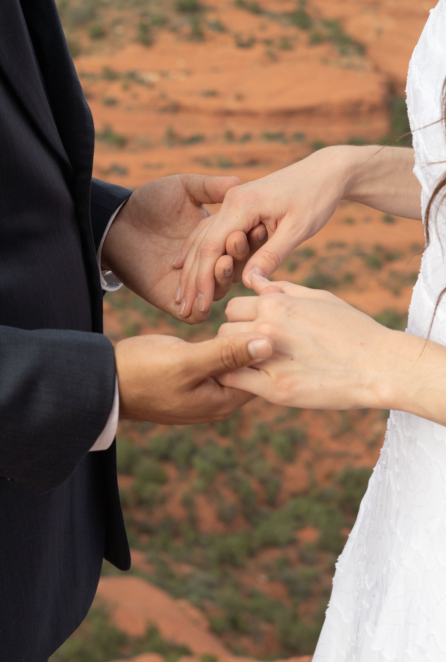 Couple exchanging wedding rings outdoors with red rock Sedona Arizona landscape in background during ceremony.