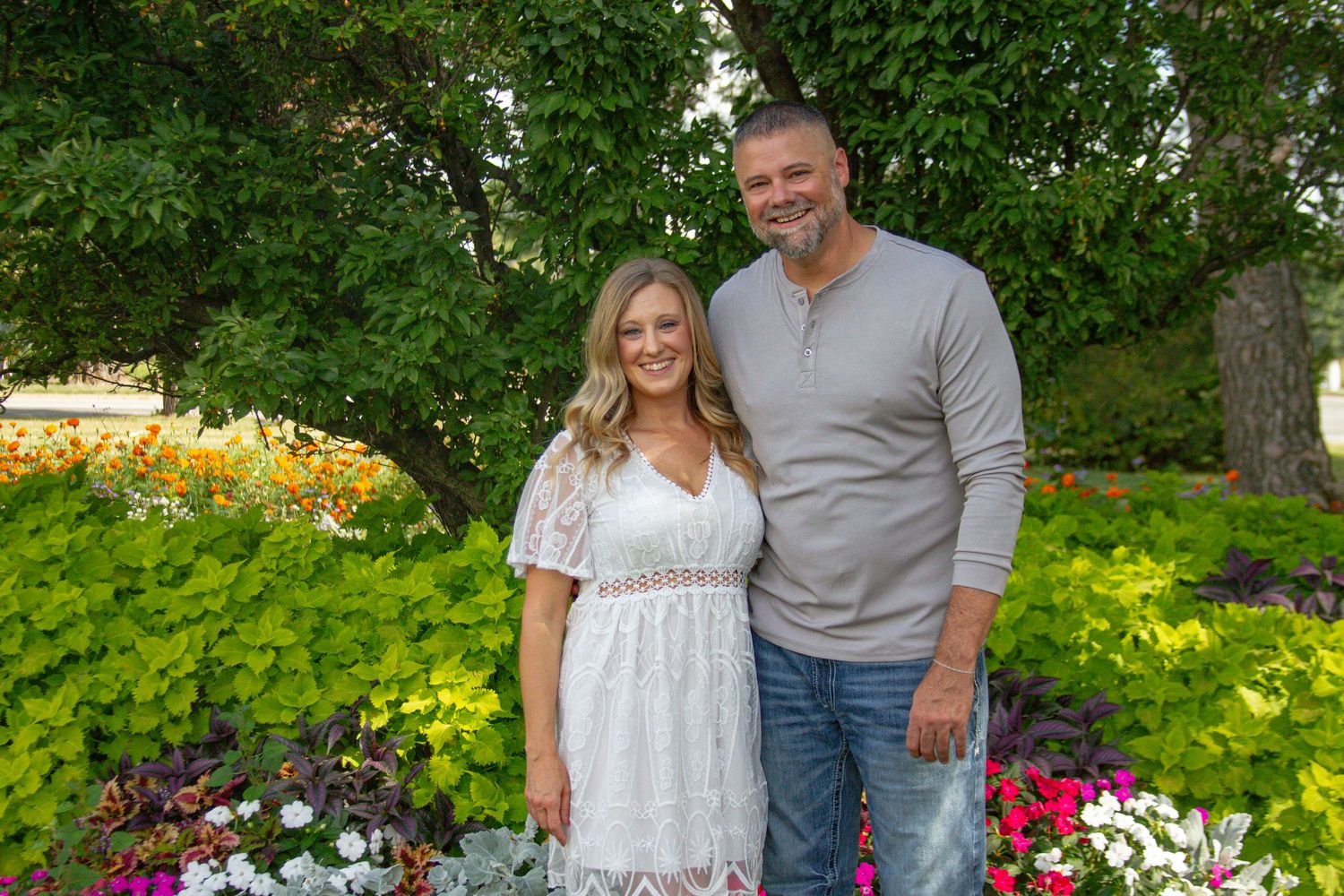 A couple stands together in a garden with colorful flowers blooming in the background.