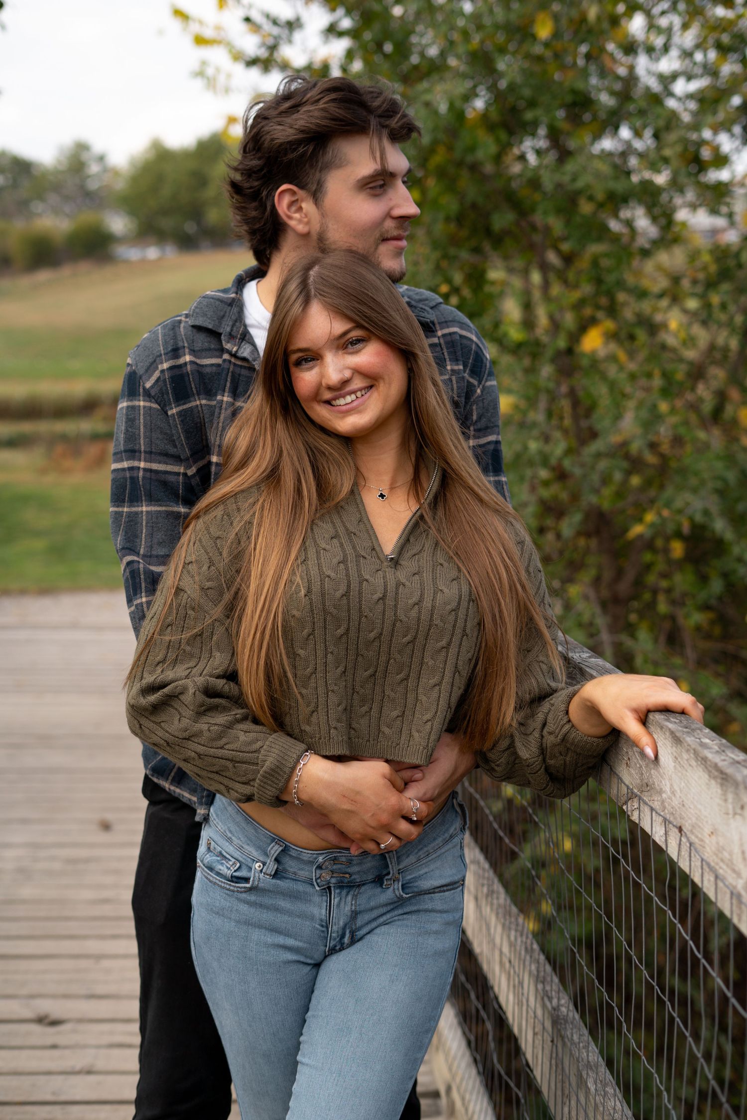 Two people share a joyful moment while posing on a wooden bridge in autumn.
