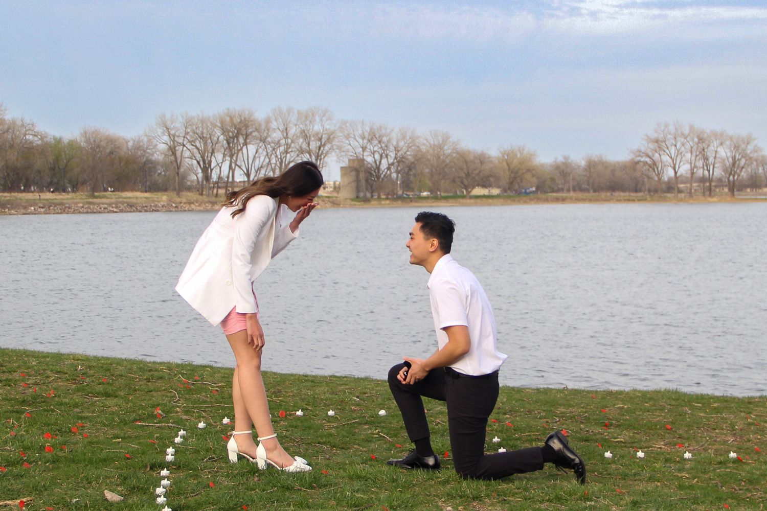 A romantic proposal scene by a lake with tea lights arranged on the grass.