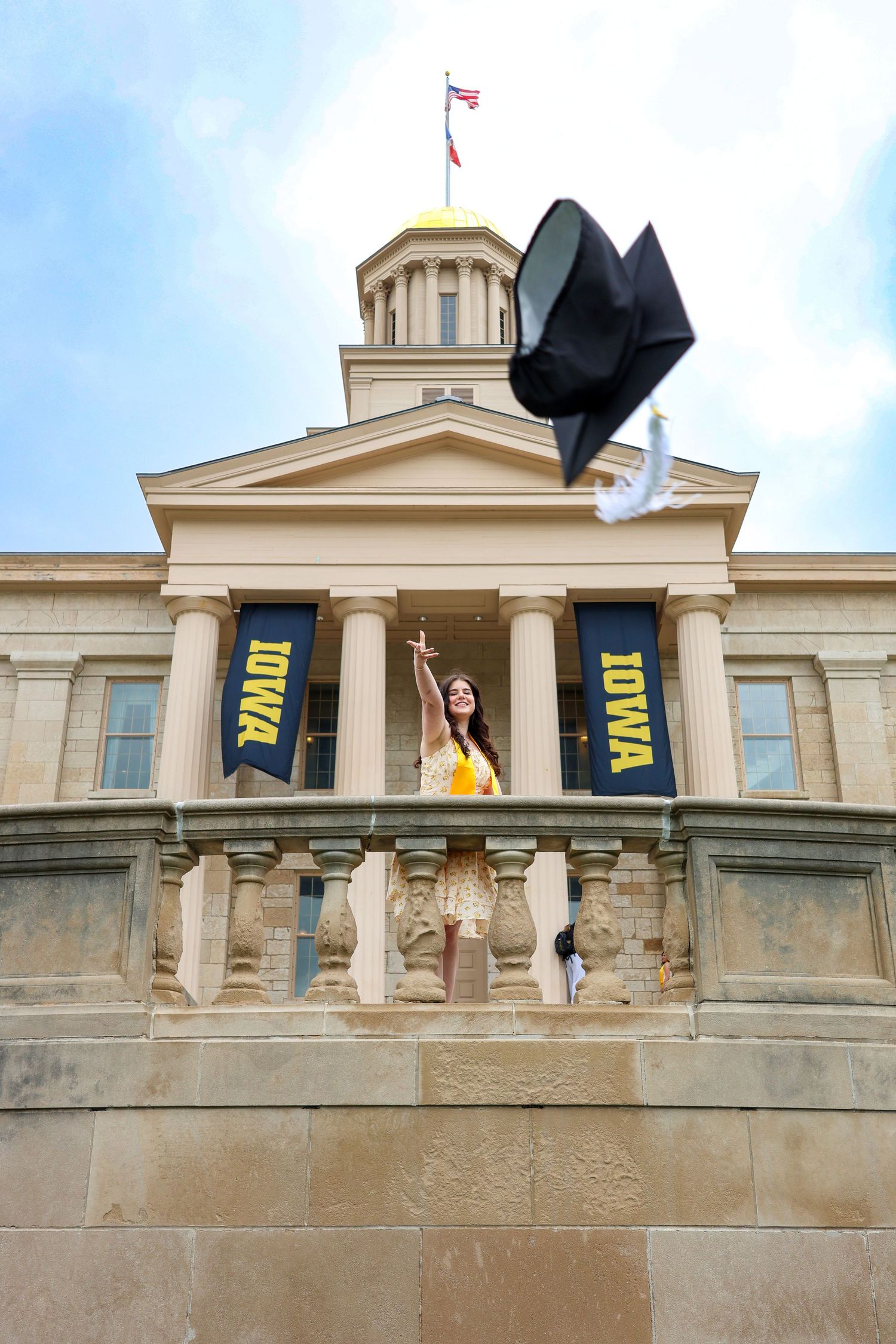 Graduation cap toss photographed against Iowa Old Capitol building with yellow banners displayed.