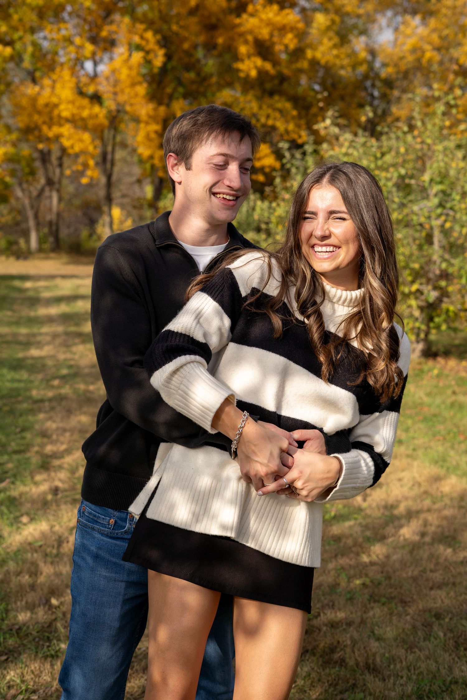 A playful couple in contrasting black and white sweaters enjoy a fun moment in an autumn park.