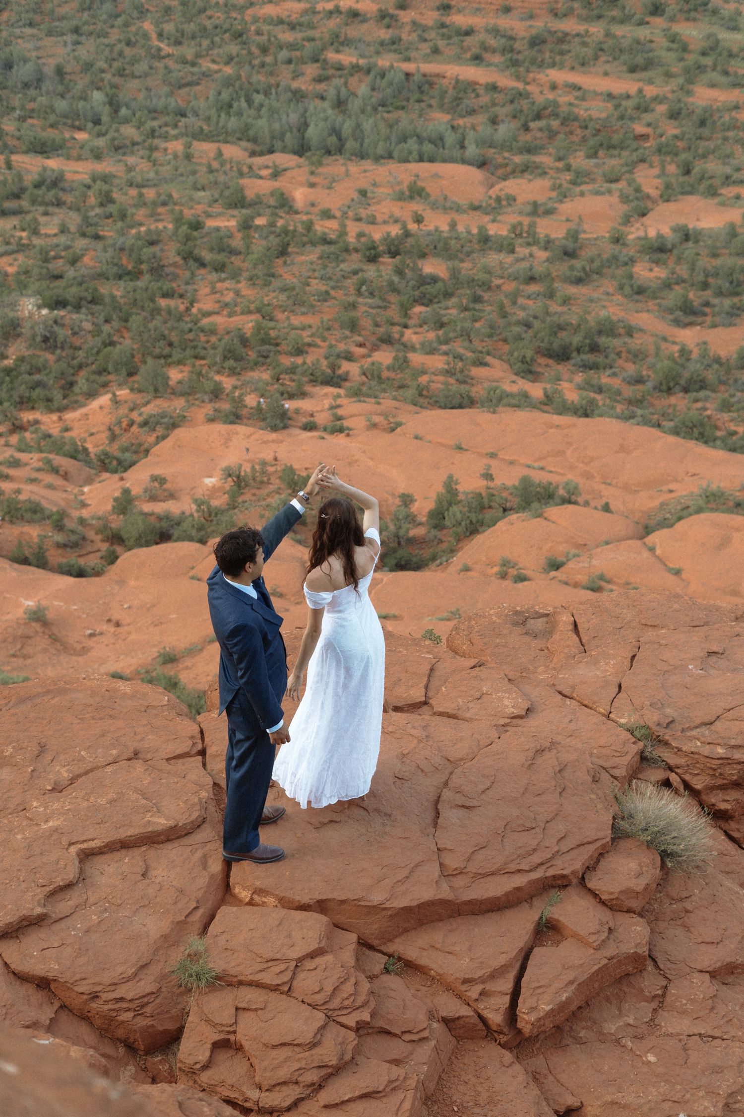 Couple in wedding attire dancing on red rock formations in Sedona, Arizona desert landscape.