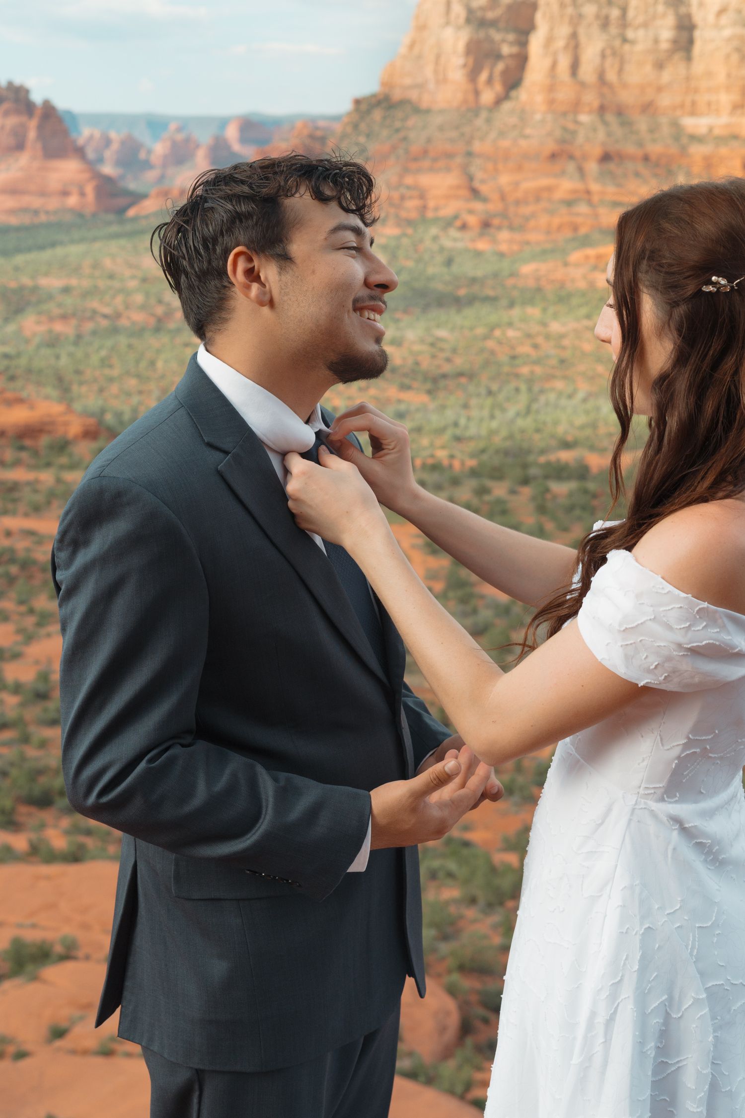 Bride adjusting groom's bow tie with red rock Sedona Arizona landscape in background during outdoor wedding.