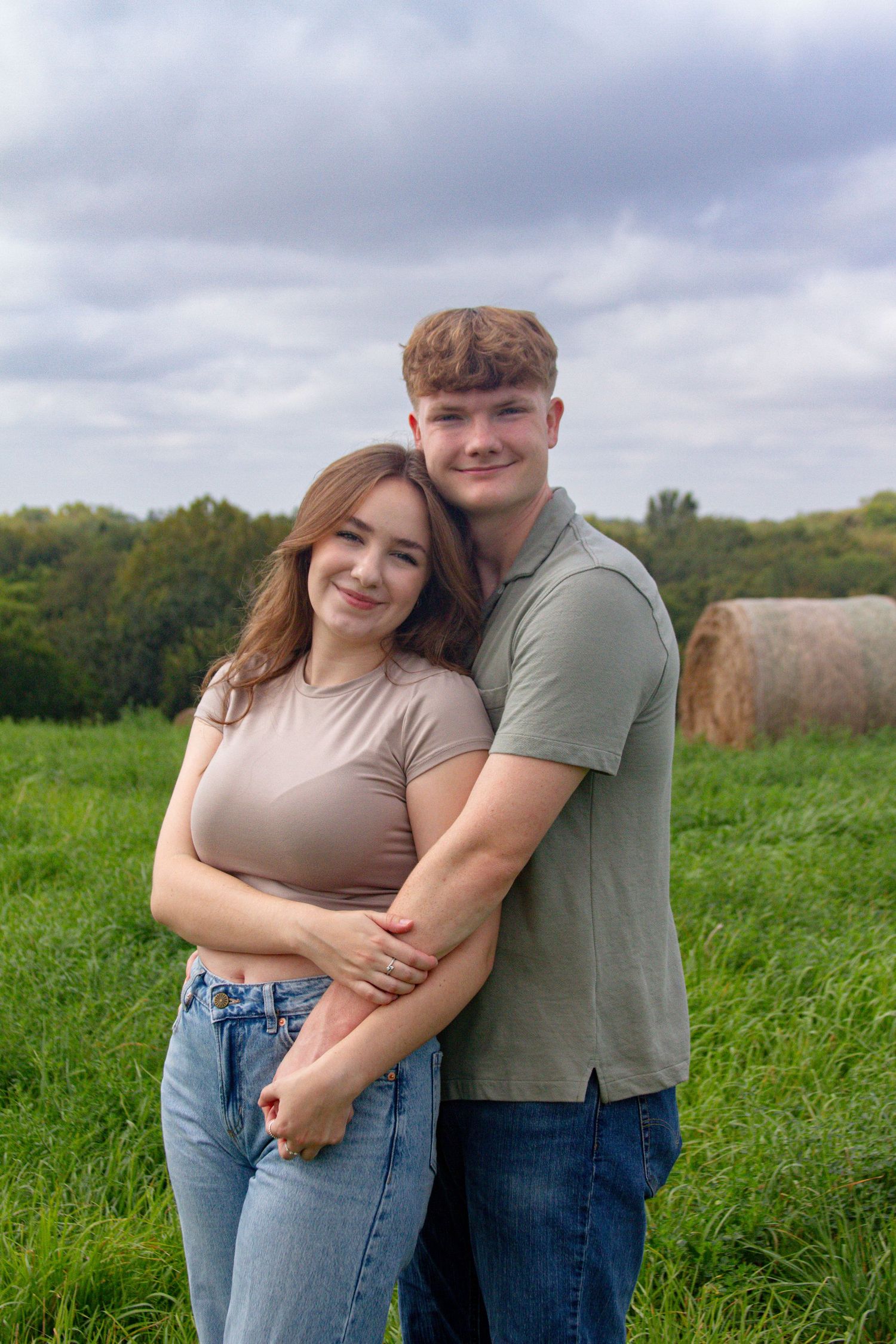 A couple sharing an intimate moment while posing in a lush green field.