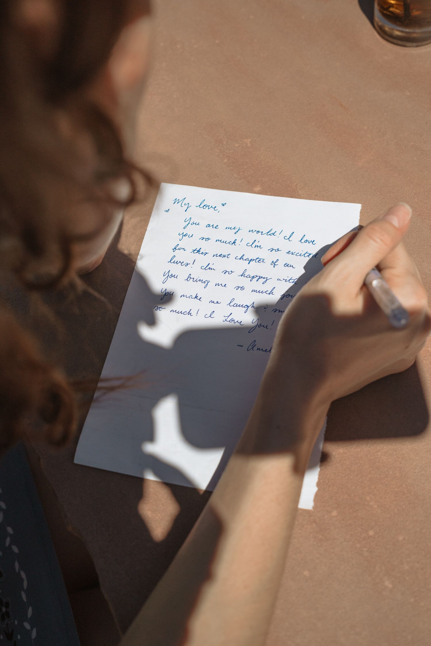 Woman reading a handwritten love letter outdoors in sunlight, holding pen with shadow cast on paper.