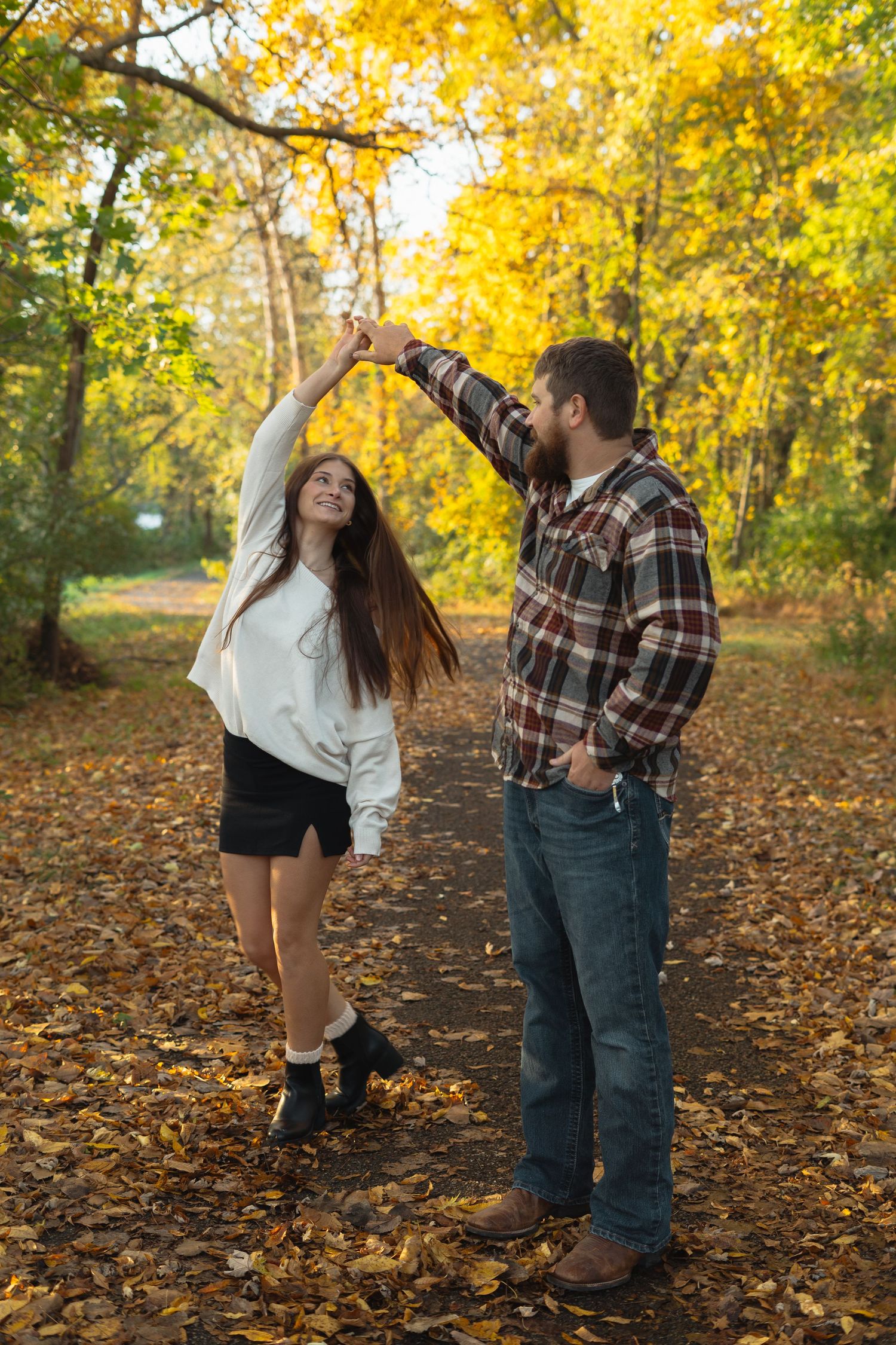 Couple sharing playful moments in autumn park with golden foliage scattered on ground.