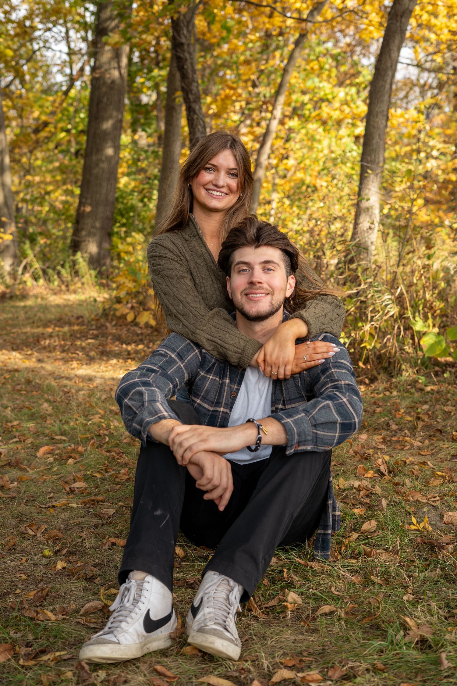 Two people share a candid moment while sitting on autumn leaves in a park.