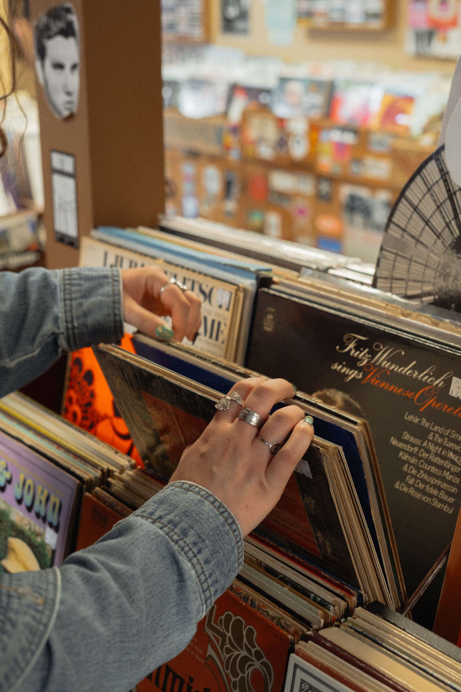 Hands flipping through vinyl records in a music store with denim sleeves visible.
