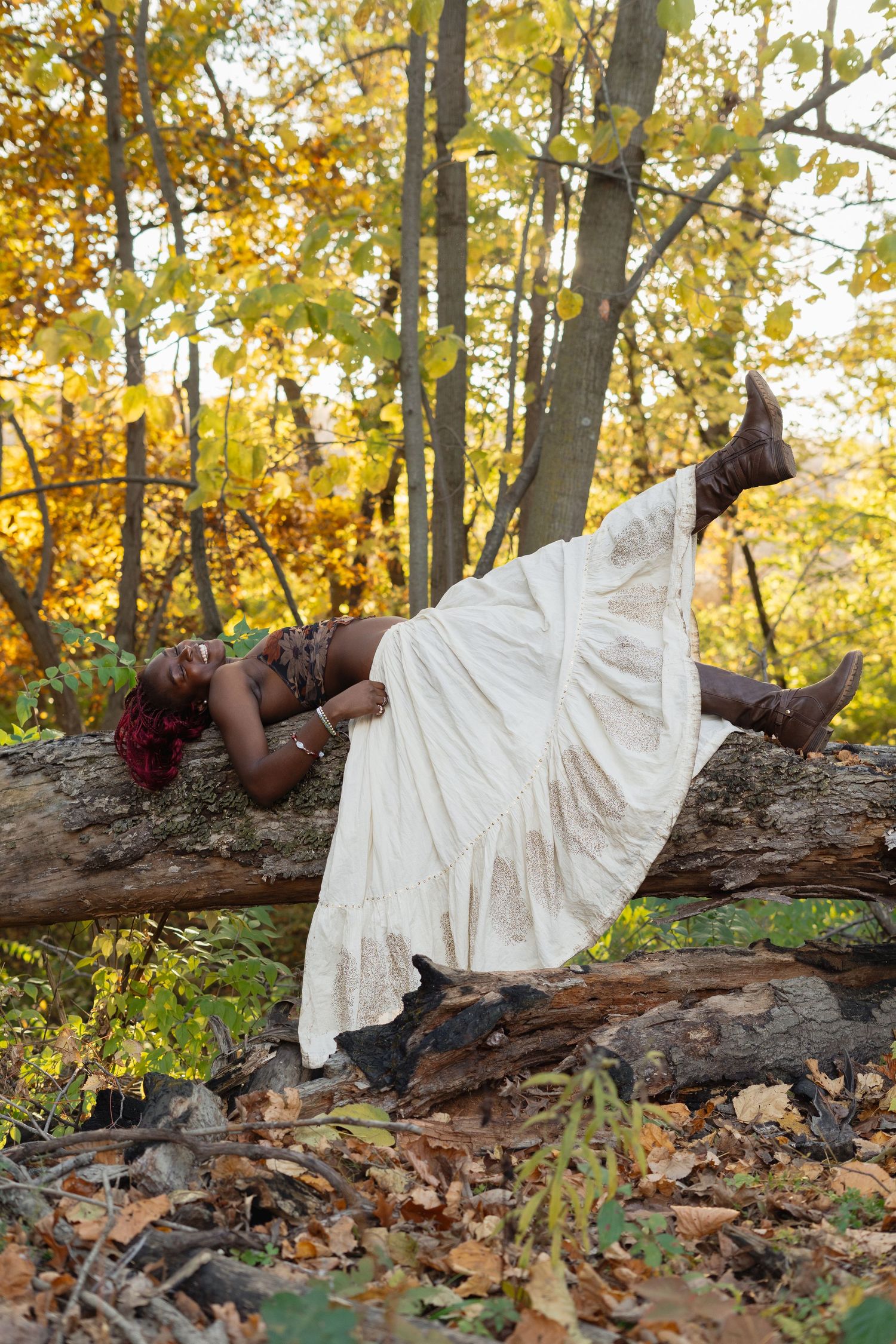 A white dress lays draped across a fallen log in an autumn forest with golden leaves in the background.