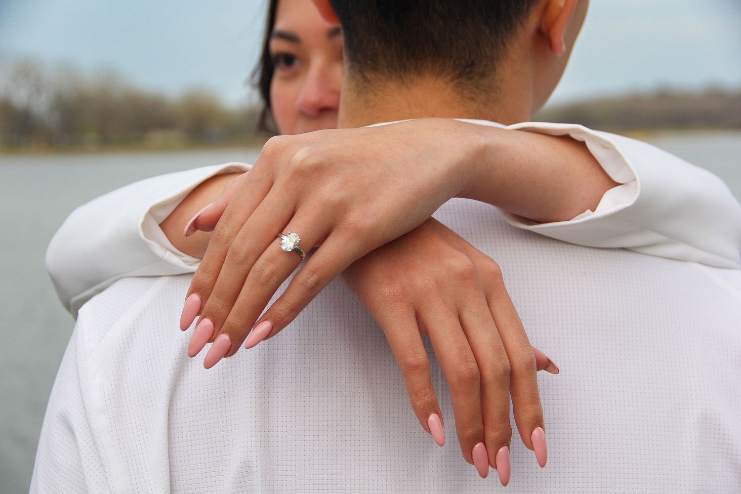 Close-up view of hands with pink manicured nails and an engagement ring embracing in a loving hug outdoors.