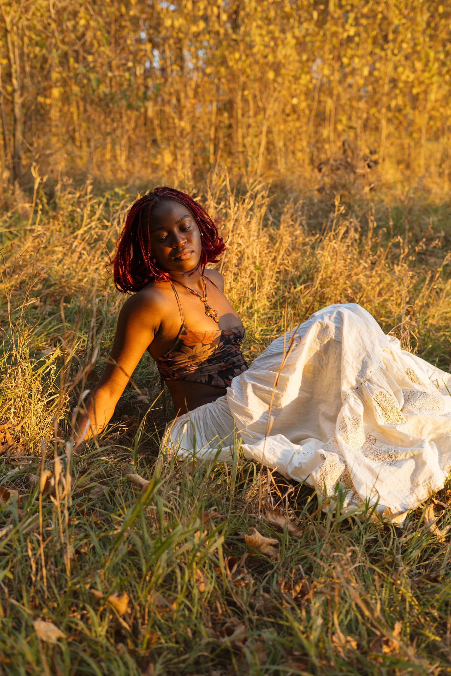 A person in a white dress lies gracefully in a golden field of tall grass during sunset.