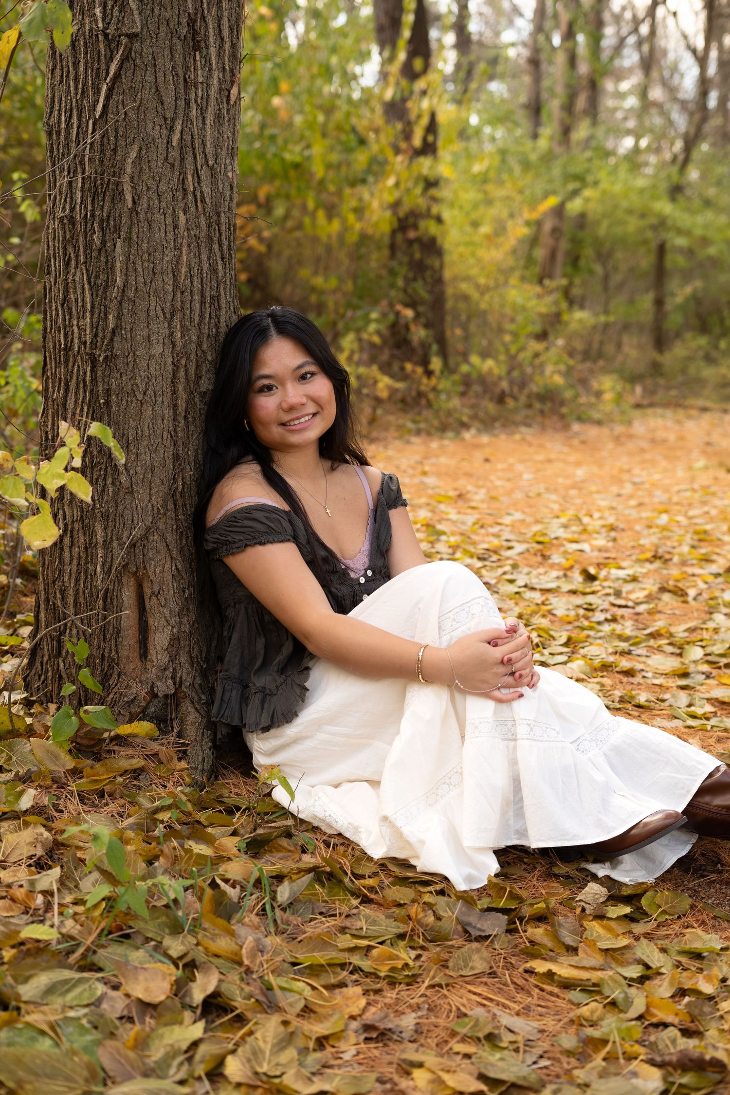 A maternity photo taken in an autumn forest setting with fallen leaves and trees in the background.