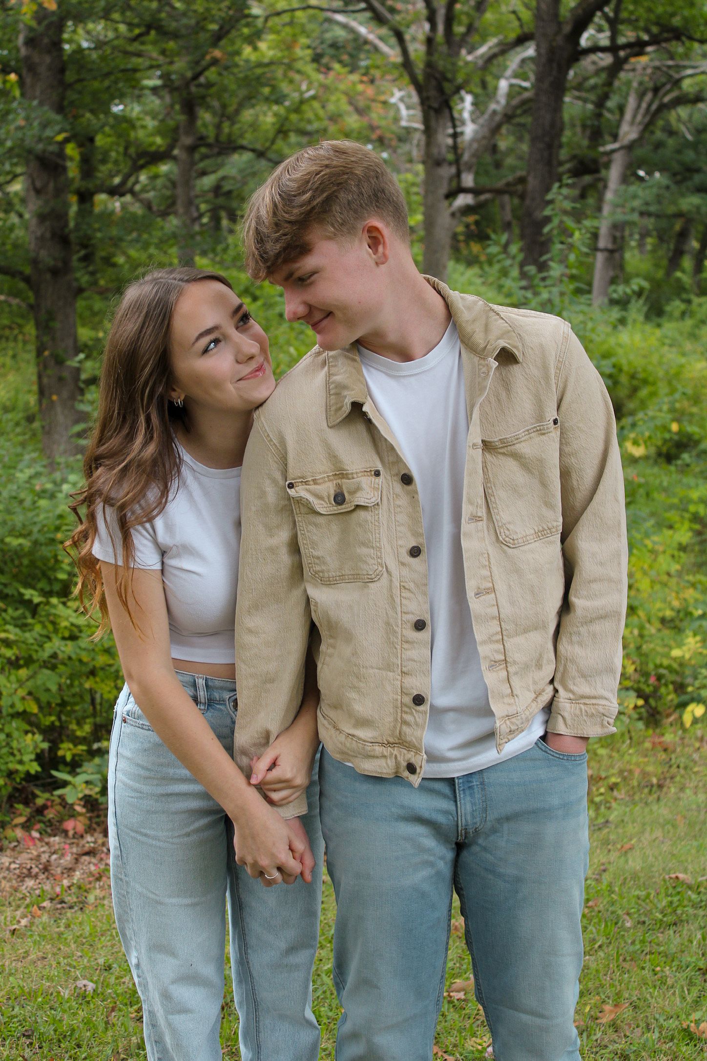A couple in matching denim and white tops share playful moments in a lush green forest setting.