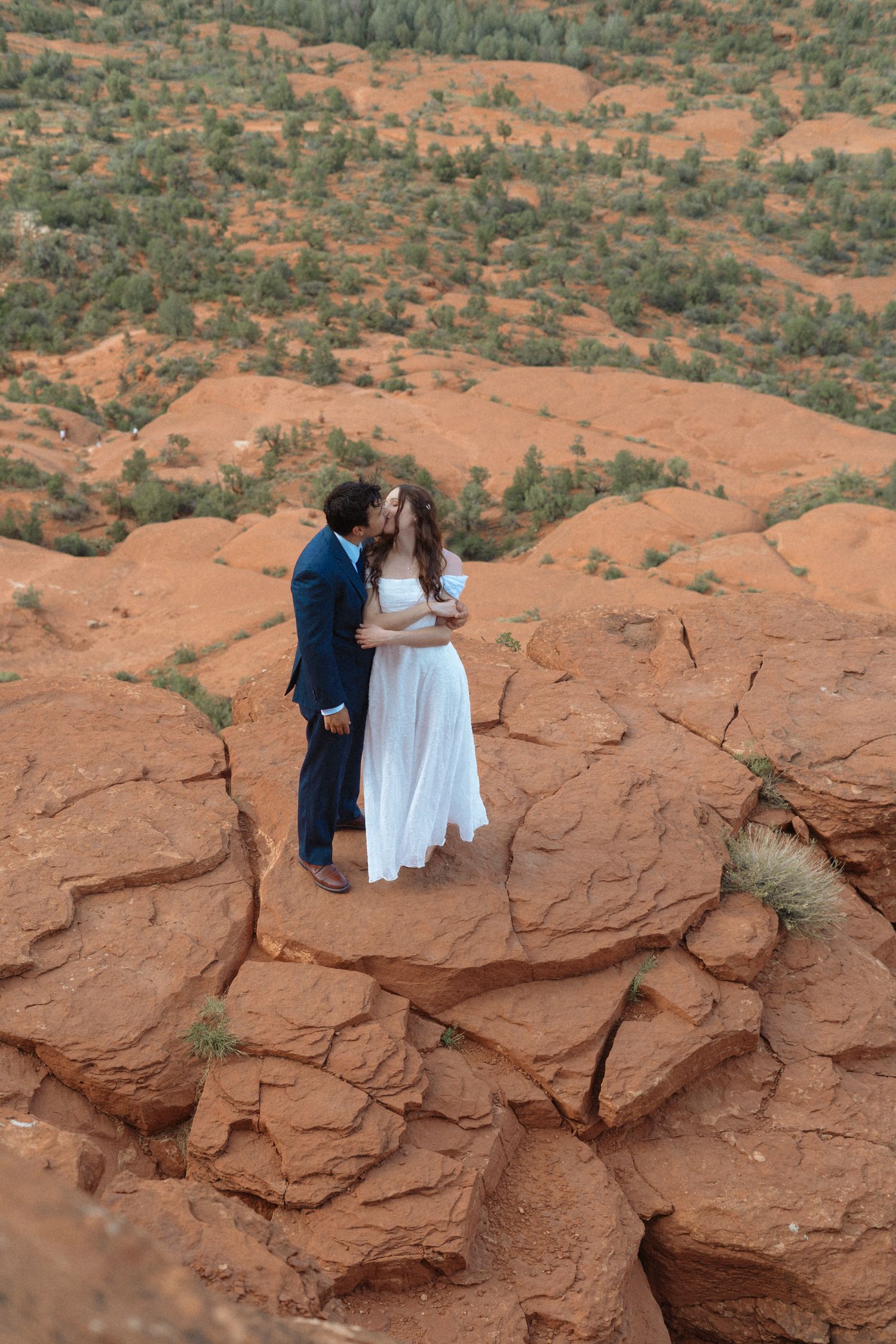Couple sharing a kiss in wedding attire on red rock formations in Sedona, Arizona desert landscape.
