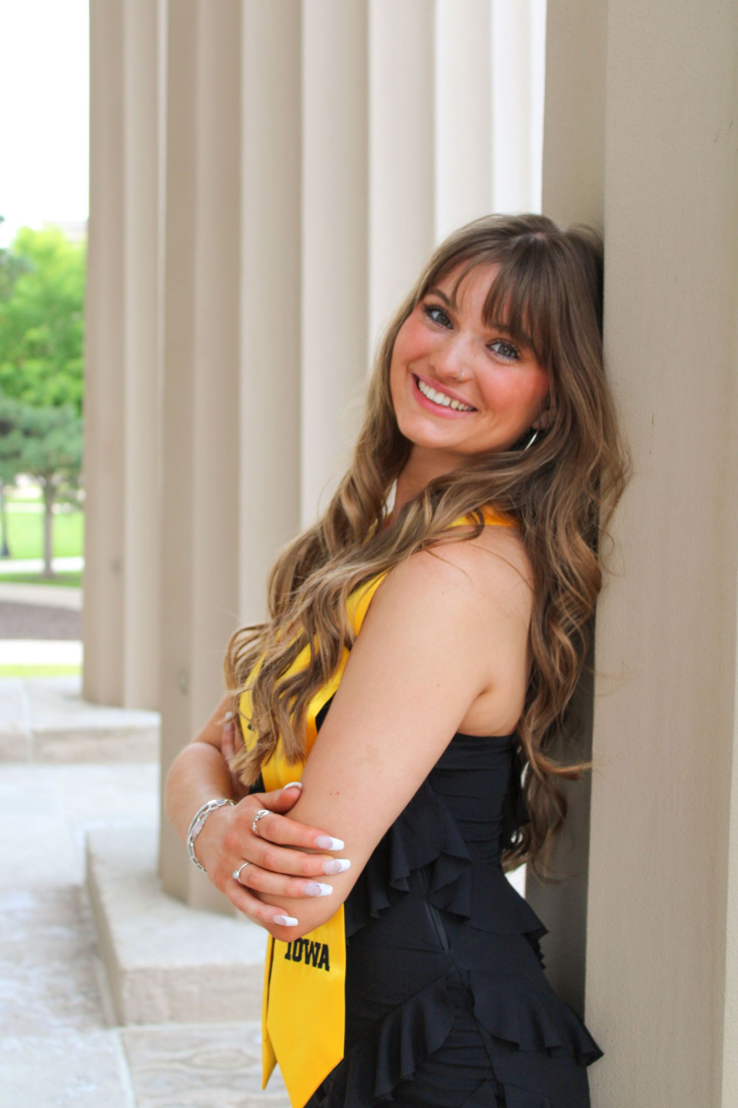 Graduate in black dress and yellow stole posing between classical columns.