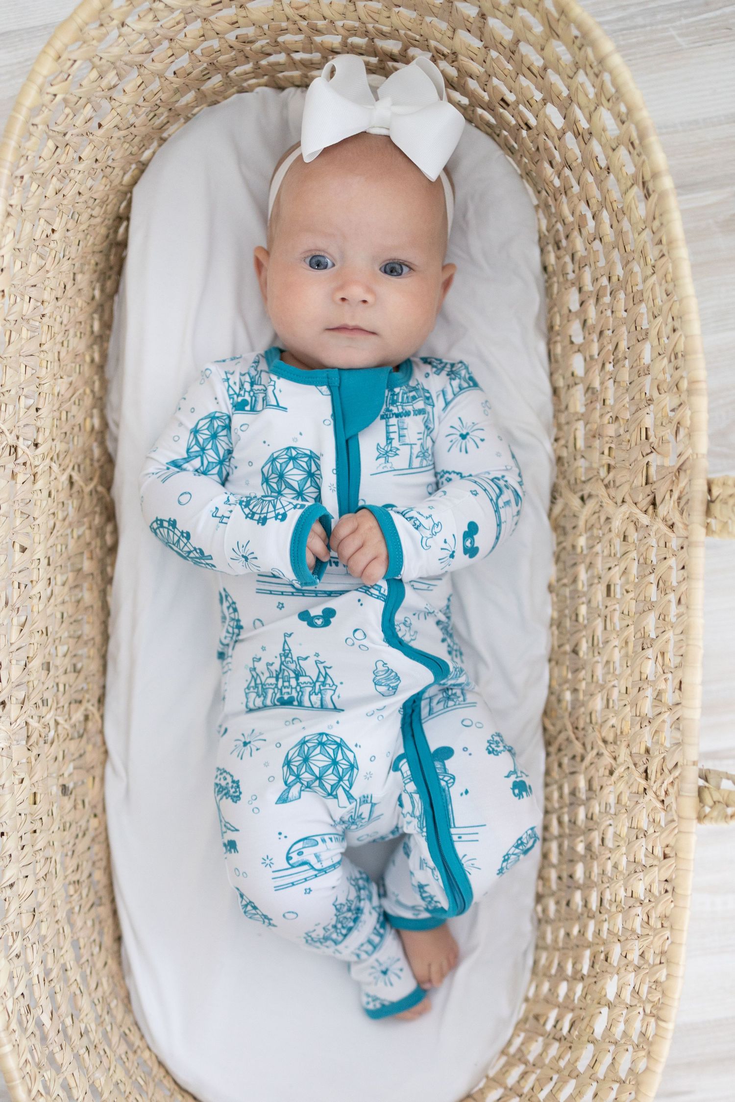 Baby in white and turquoise patterned sleepwear rests in woven basket with white lining.