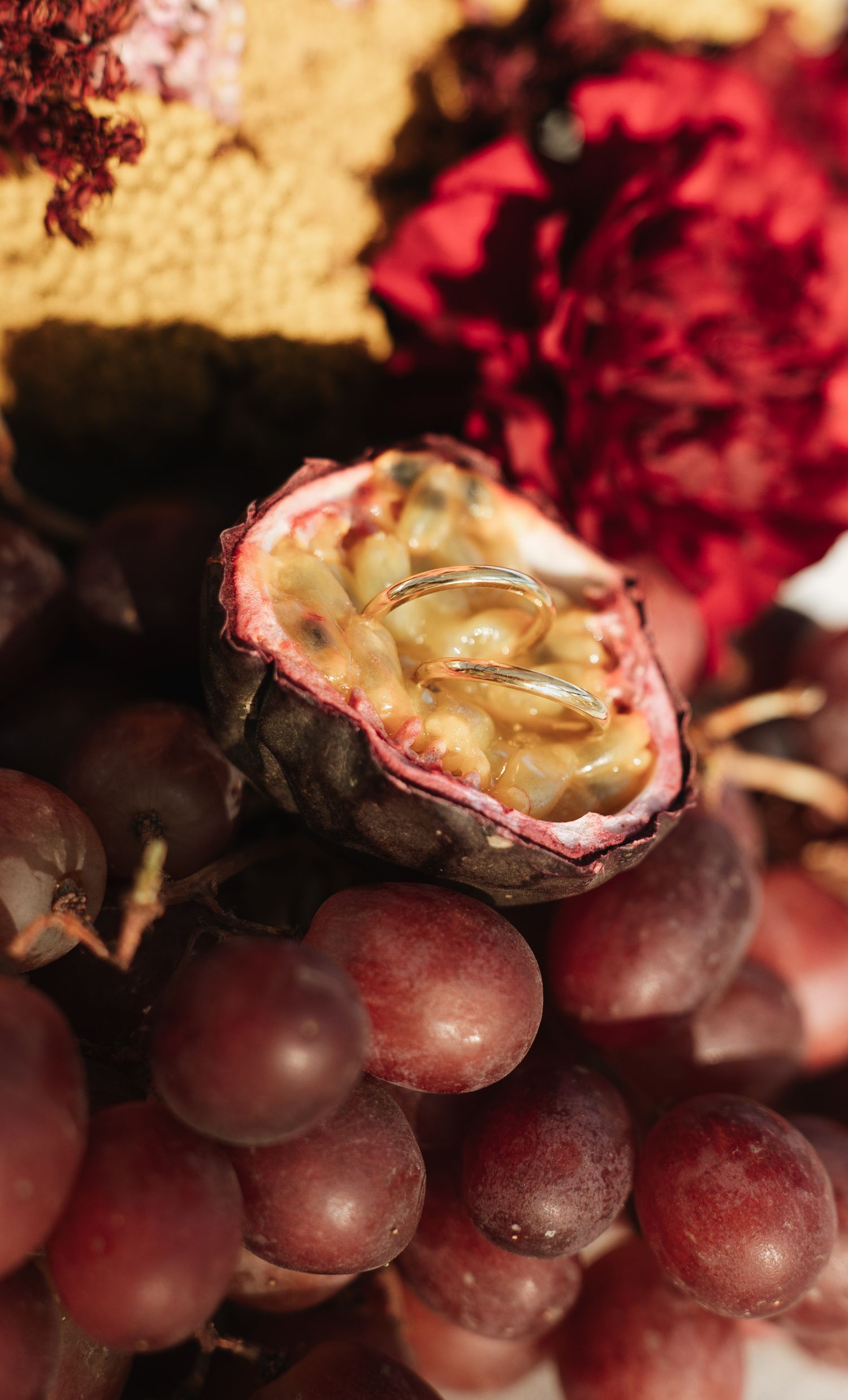 Close-up of a sliced passion fruit and red grapes with vibrant red flowers in the background.