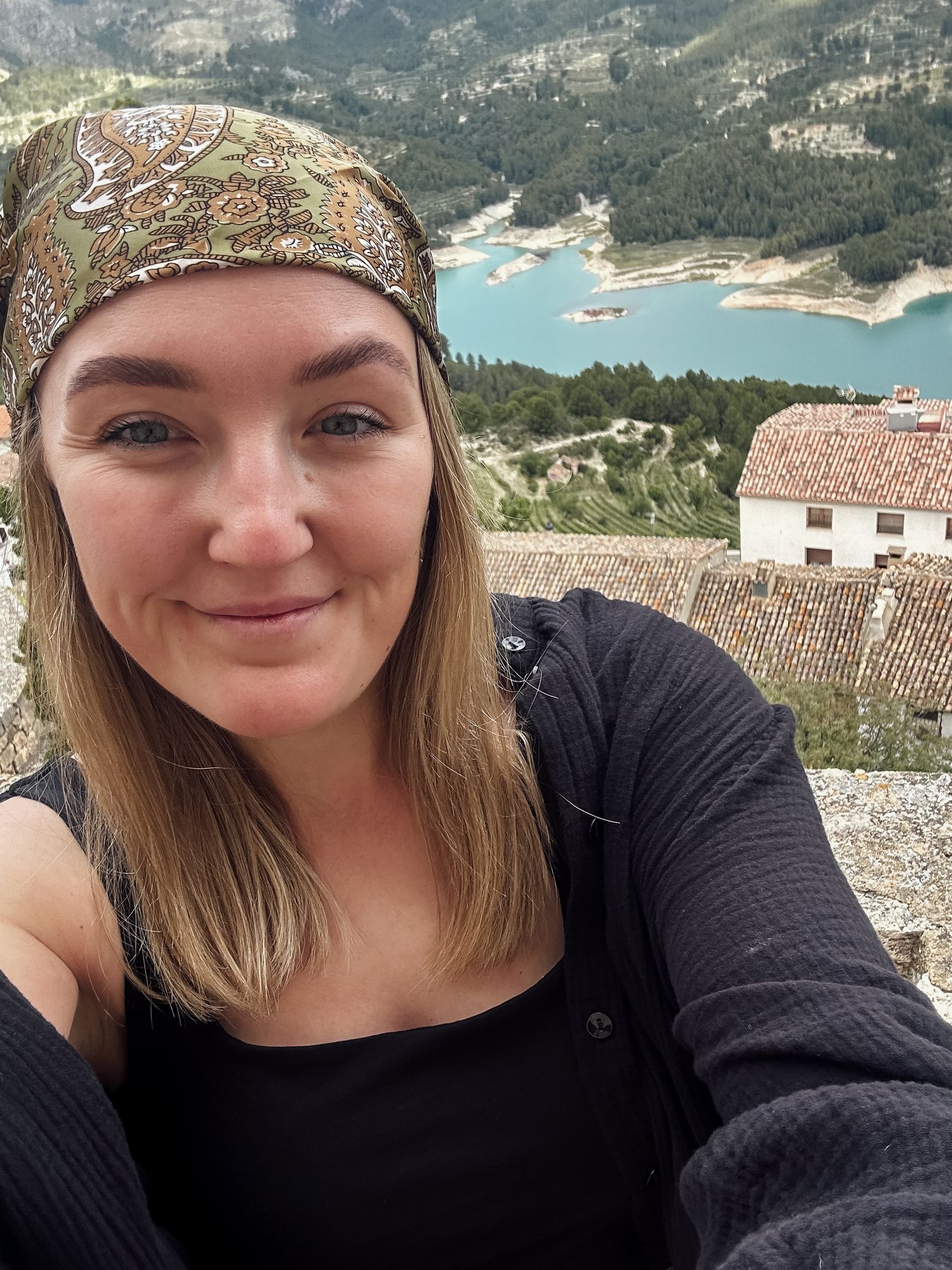 Woman taking a selfie with a scenic turquoise lake and mountain landscape in the background.