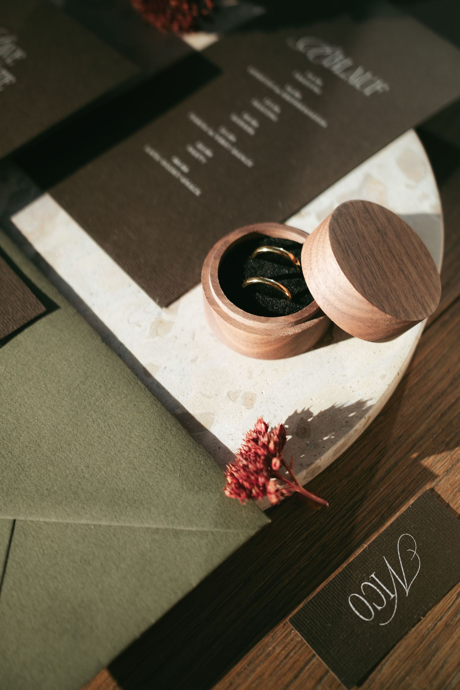 Wedding stationery and rose gold rings arranged artistically on dark surfaces with delicate floral accents.