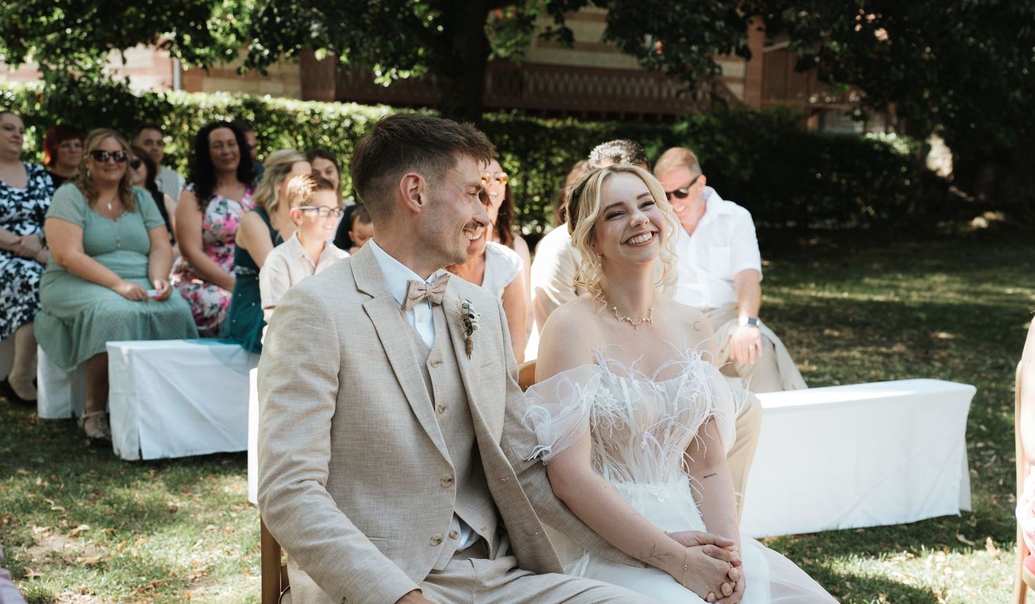 Wide shot of an outdoor wedding ceremony with guests seated under trees.