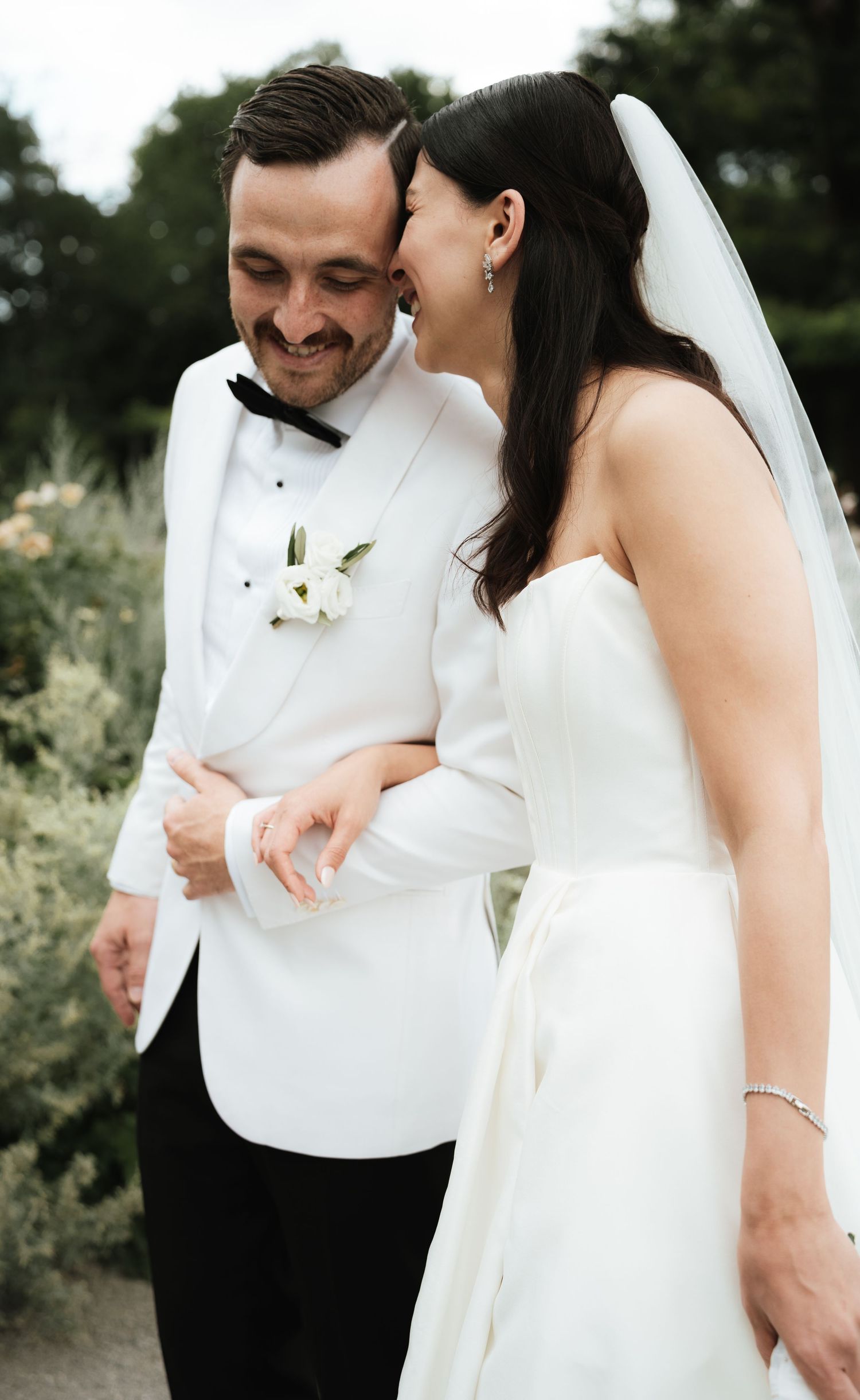 A joyful moment shared between newlyweds outdoors, with the bride in white and groom in a white tuxedo jacket.