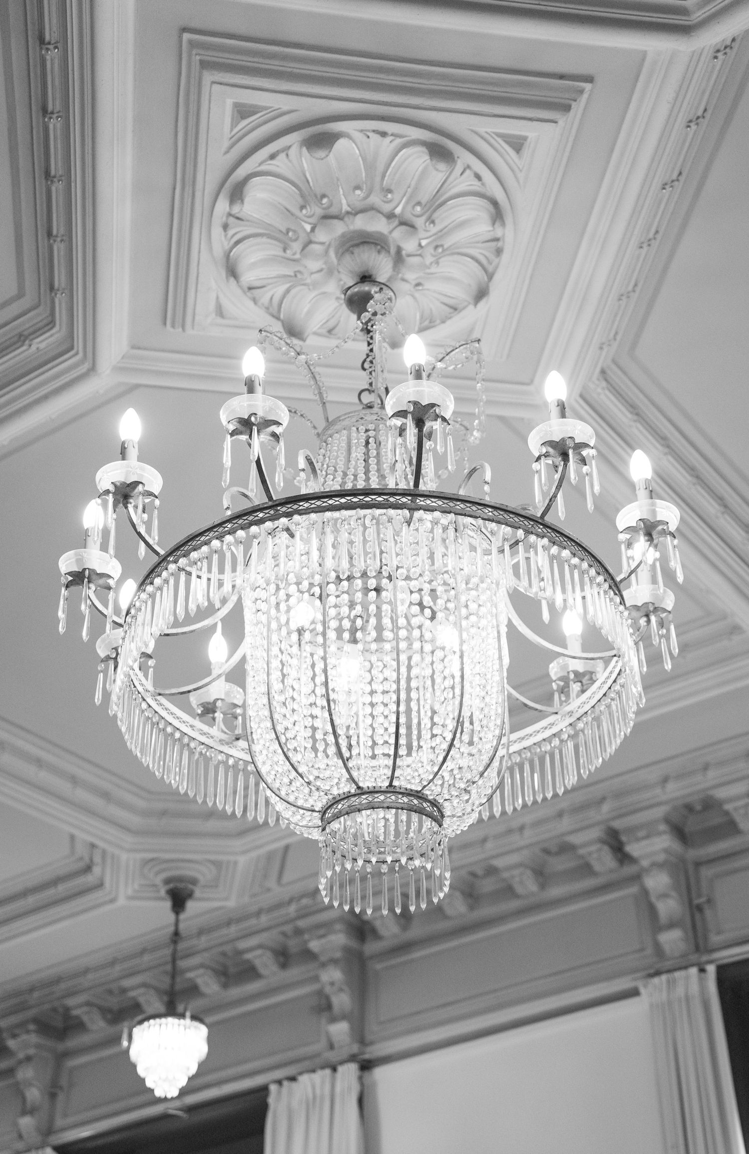 Elegant crystal chandeliers hang from an ornate white ceiling with decorative moldings in a luxurious ballroom.