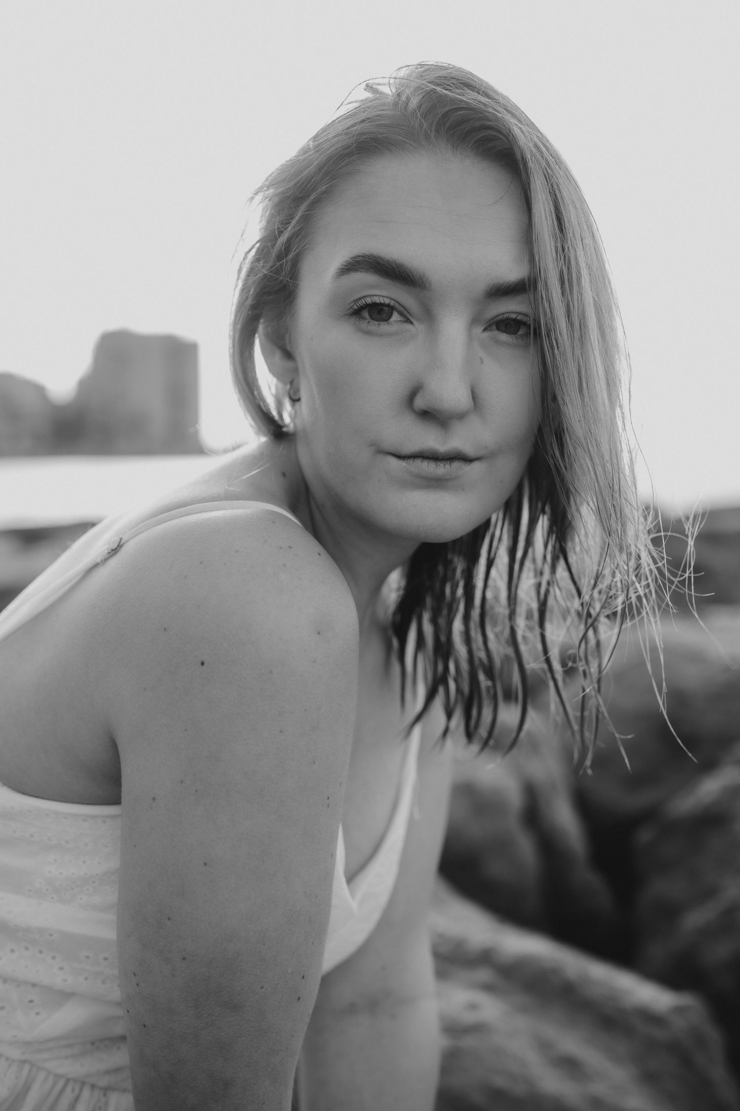 Black and white portrait of a young woman with wet hair wearing a white dress, posing outdoors near rocks.