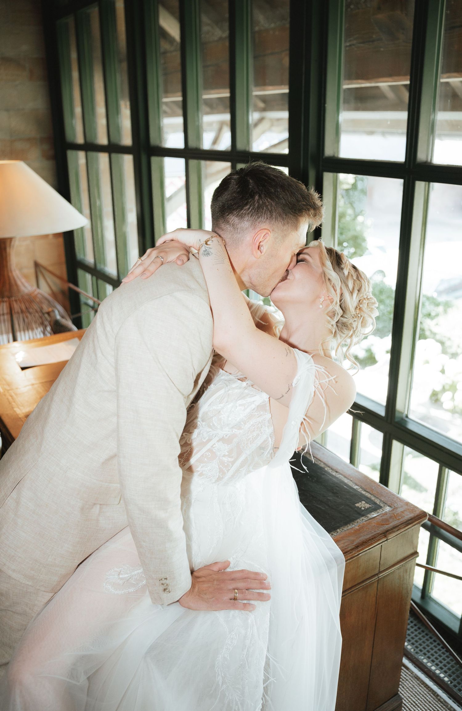 A romantic wedding couple shares intimate kisses in a series of four candid photos inside a sunlit room.