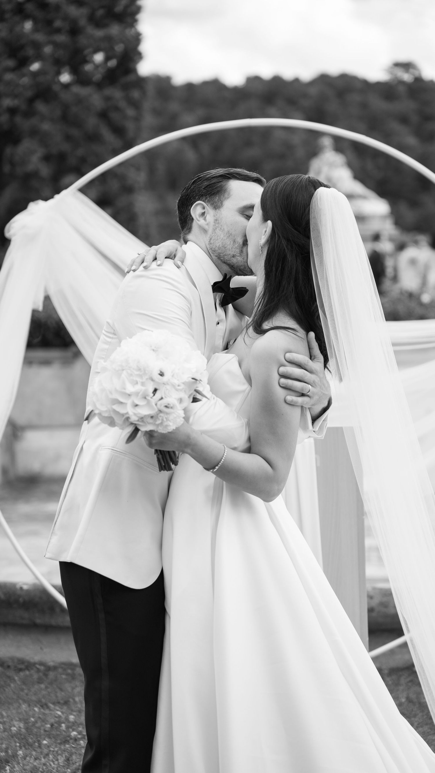 A romantic black and white wedding photo captures a couple sharing their first kiss under a flowing veil.
