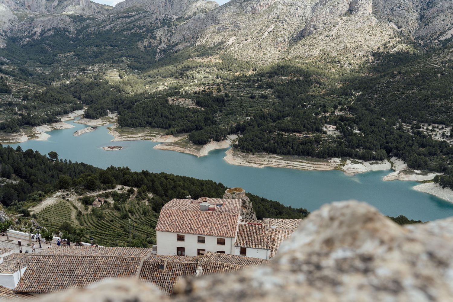 Aerial panoramic view of a mountain landscape with turquoise lake and rugged cliffs in a scenic wilderness setting.