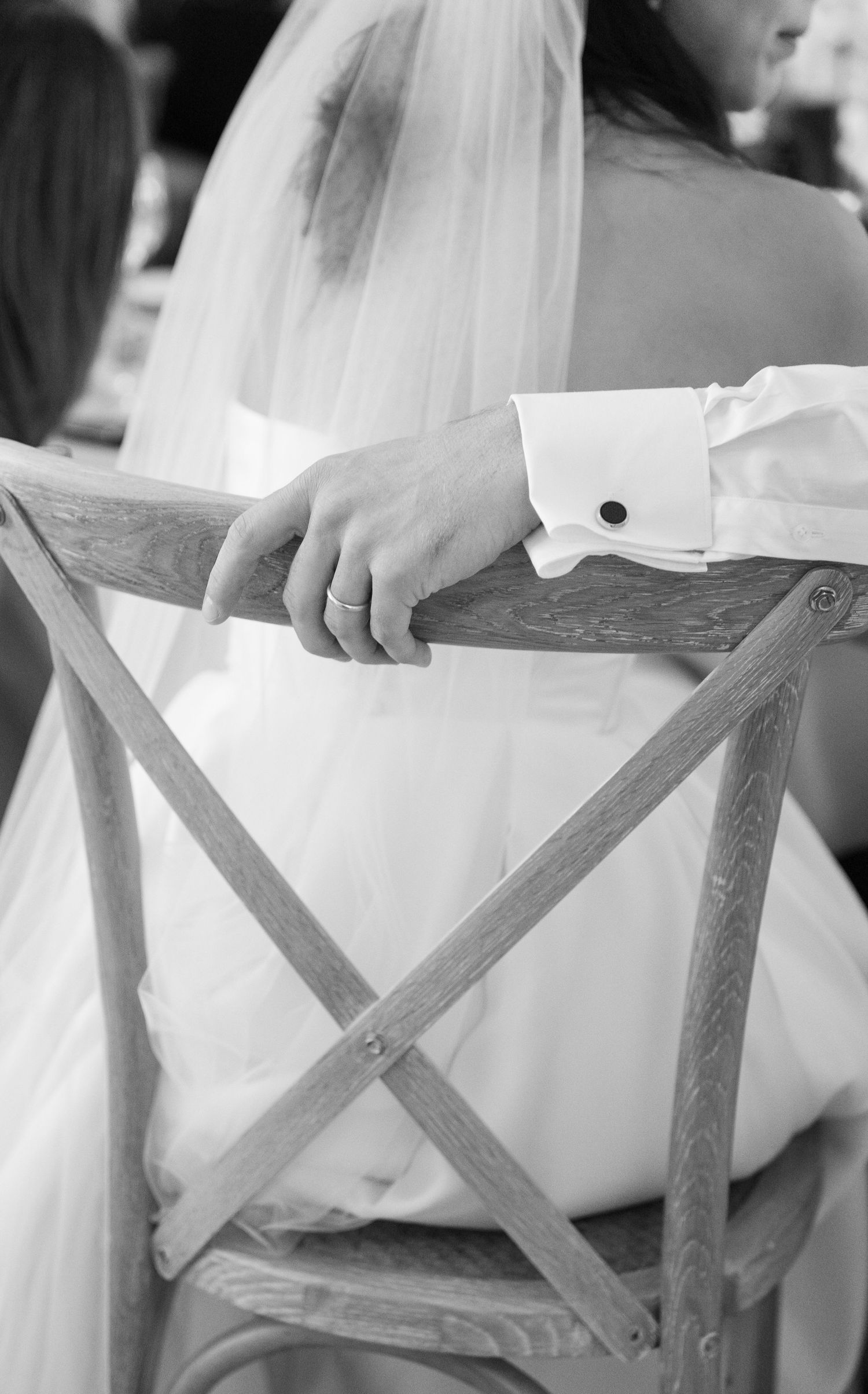 A series of black and white photos showing close-up details of a bride's white wedding dress against wooden folding chairs.