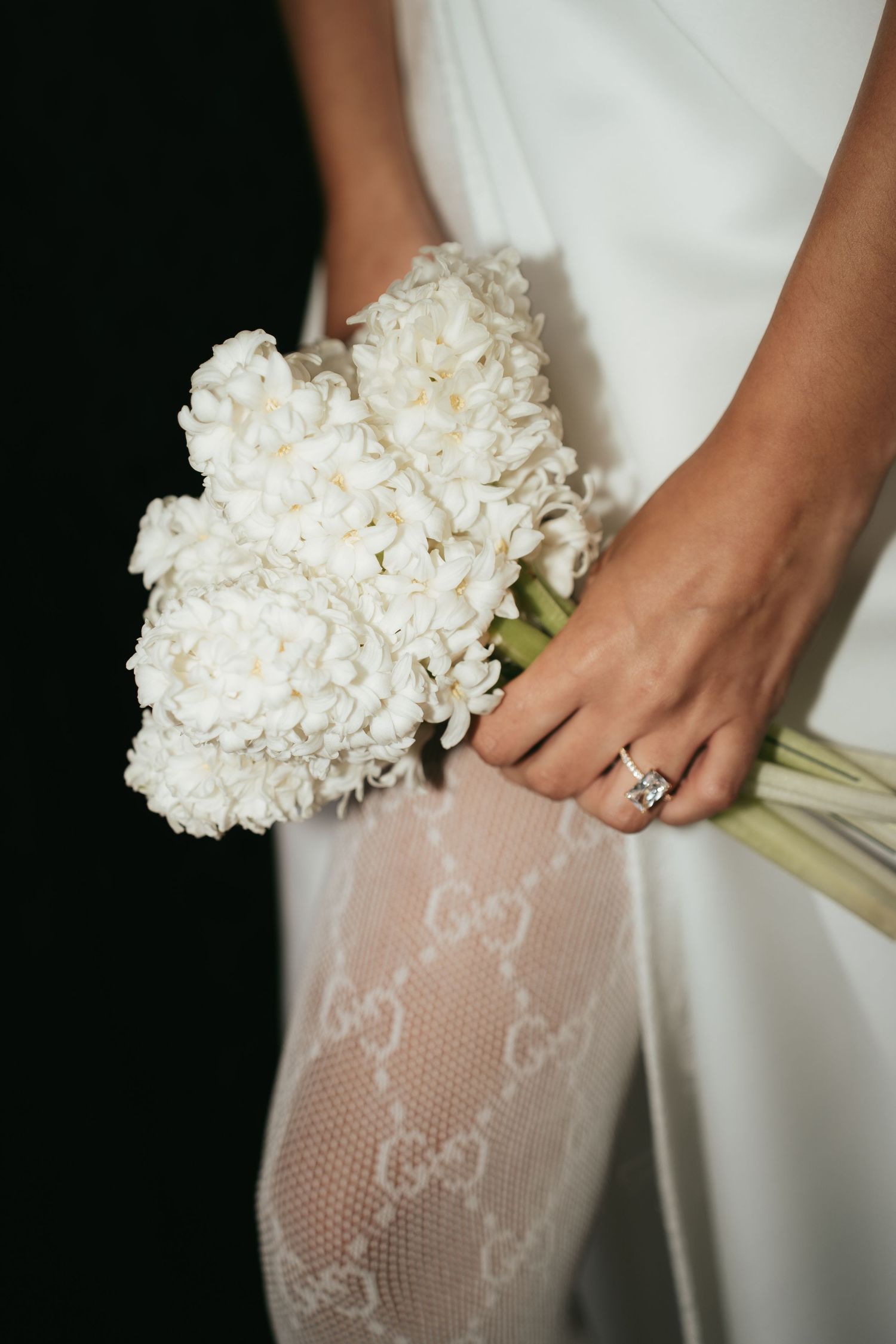 Bride holding white hydrangea bouquet wearing diamond engagement ring and Gucci lace tights in elegant wedding attire.