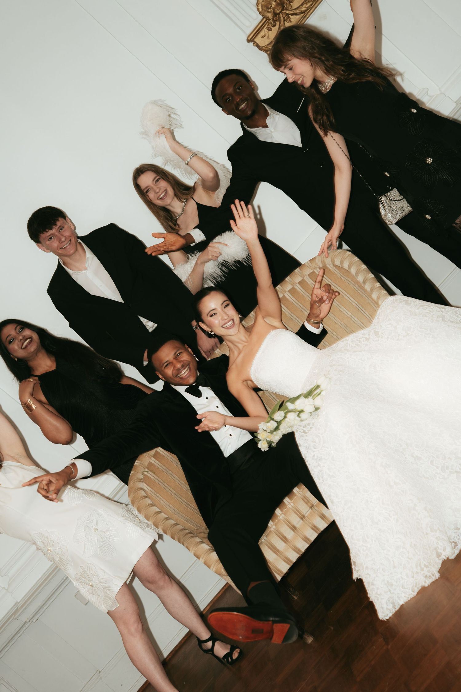 Joyful wedding party in formal attire celebrating with raised arms and smiles in an elegant white room.
