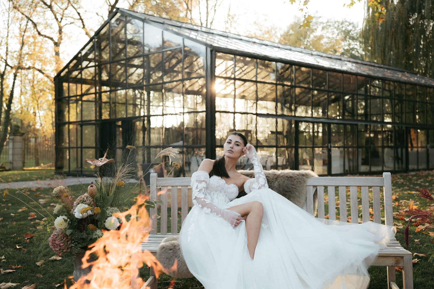 A couple in wedding attire poses in front of a greenhouse structure during sunset creating a romantic atmosphere.